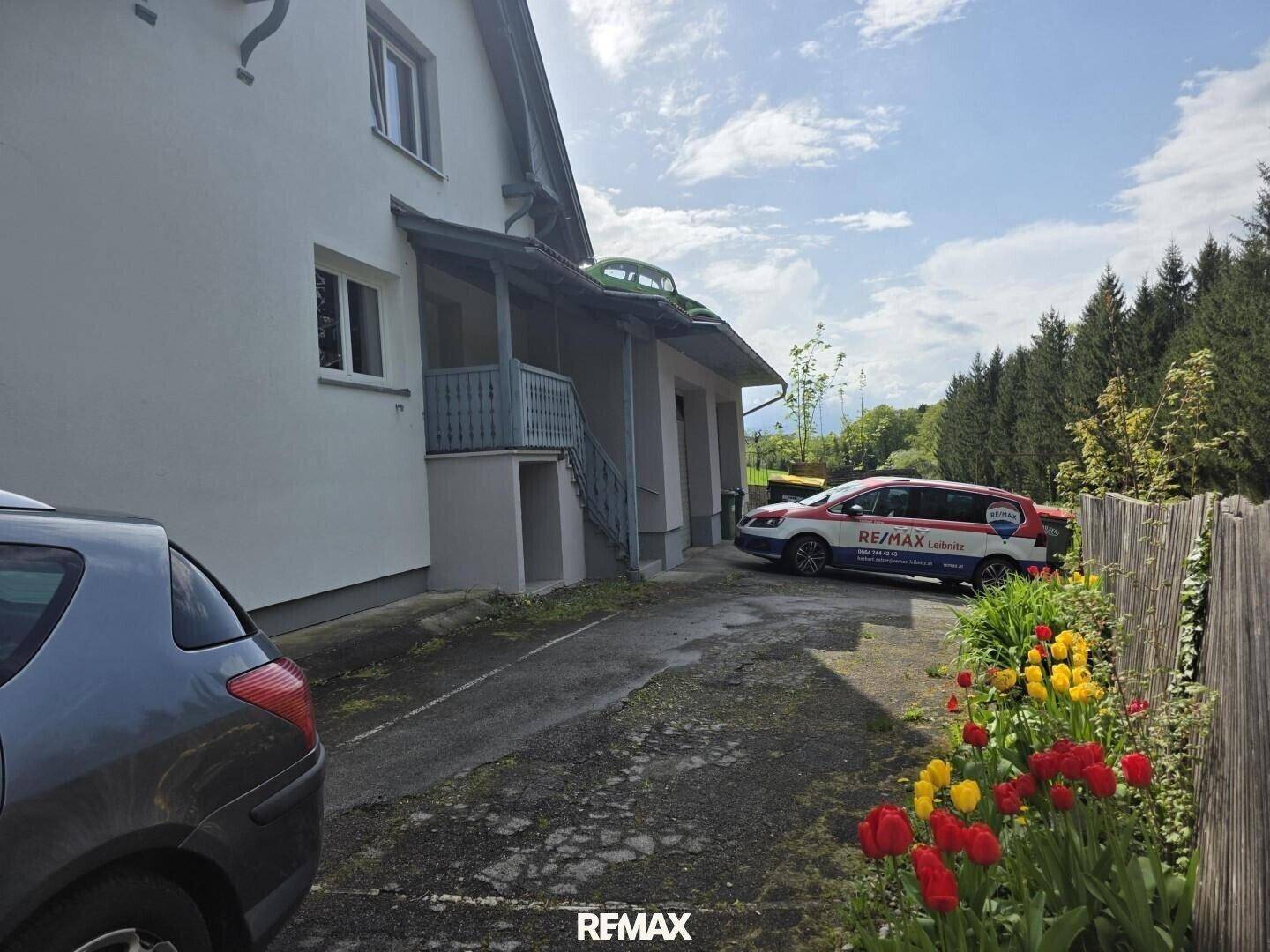 Seitenansicht des Hauses mit Außentreppe, geparktem Auto und blühenden Tulpen im Vorgarten.