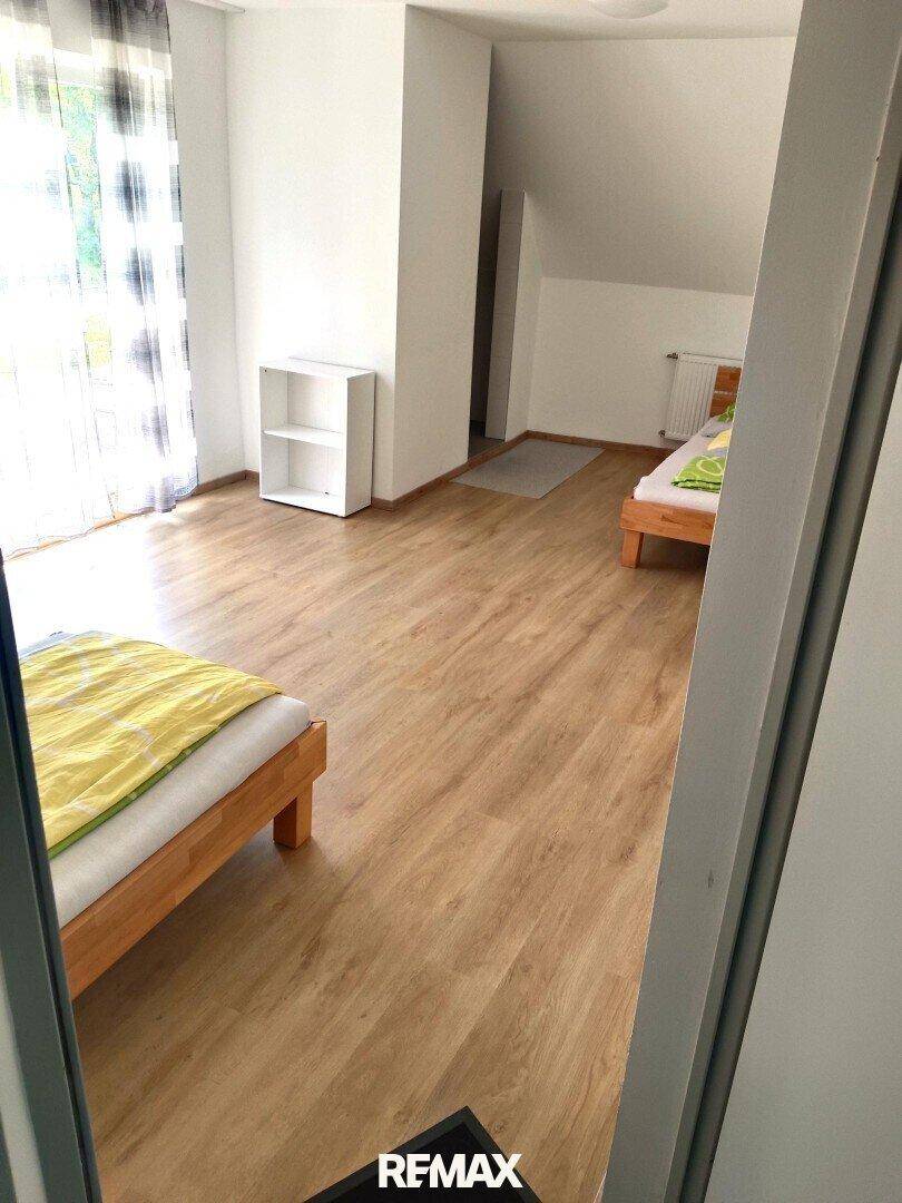 Geräumiges Schlafzimmer mit zwei Einzelbetten, Laminatboden und Zugang zu einem Balkon.