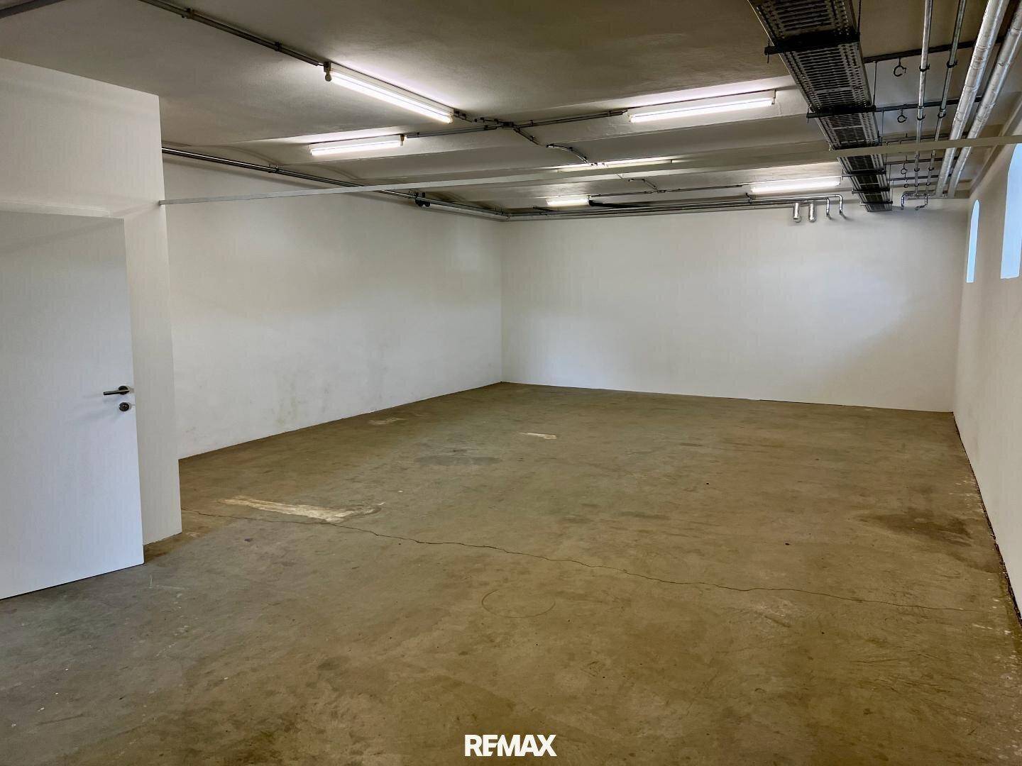 Heller, leerer Raum mit Betonboden, weißen Wänden und einer einfachen Tür, ideal für gewerbliche Nutzung.