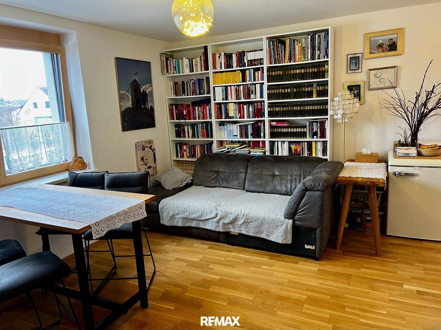 Geräumiger Wohn- und Essbereich mit Holzboden, großem Bücherregal und bequemer Couch.