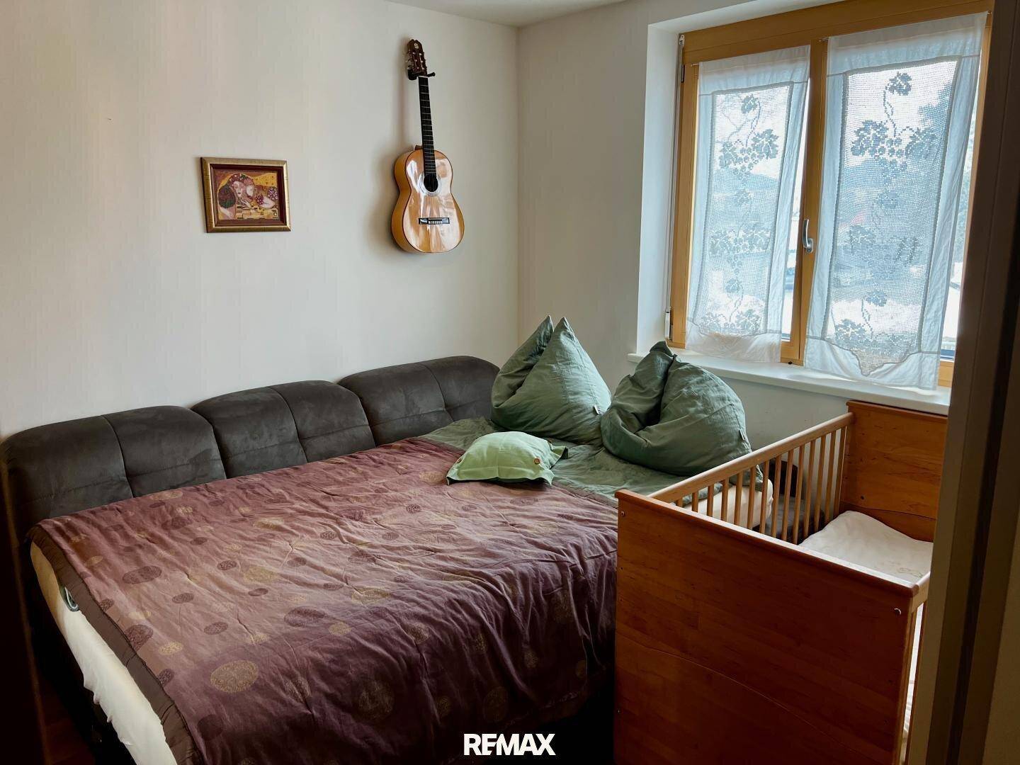 Gemütliches Schlafzimmer mit Bett, Babybett und Fenster, dekoriert mit einer Gitarre an der Wand.