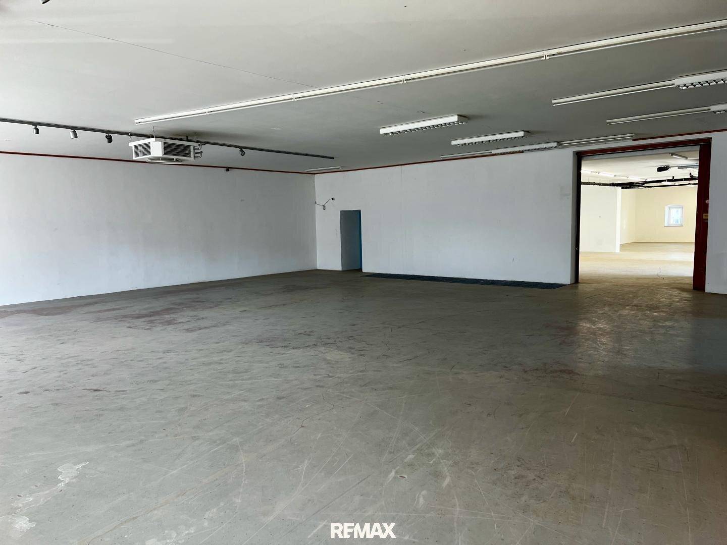 Weitläufiger, heller Gewerberaum mit hohen Decken und einem robusten Betonboden, ideal für verschiedene Nutzungen.