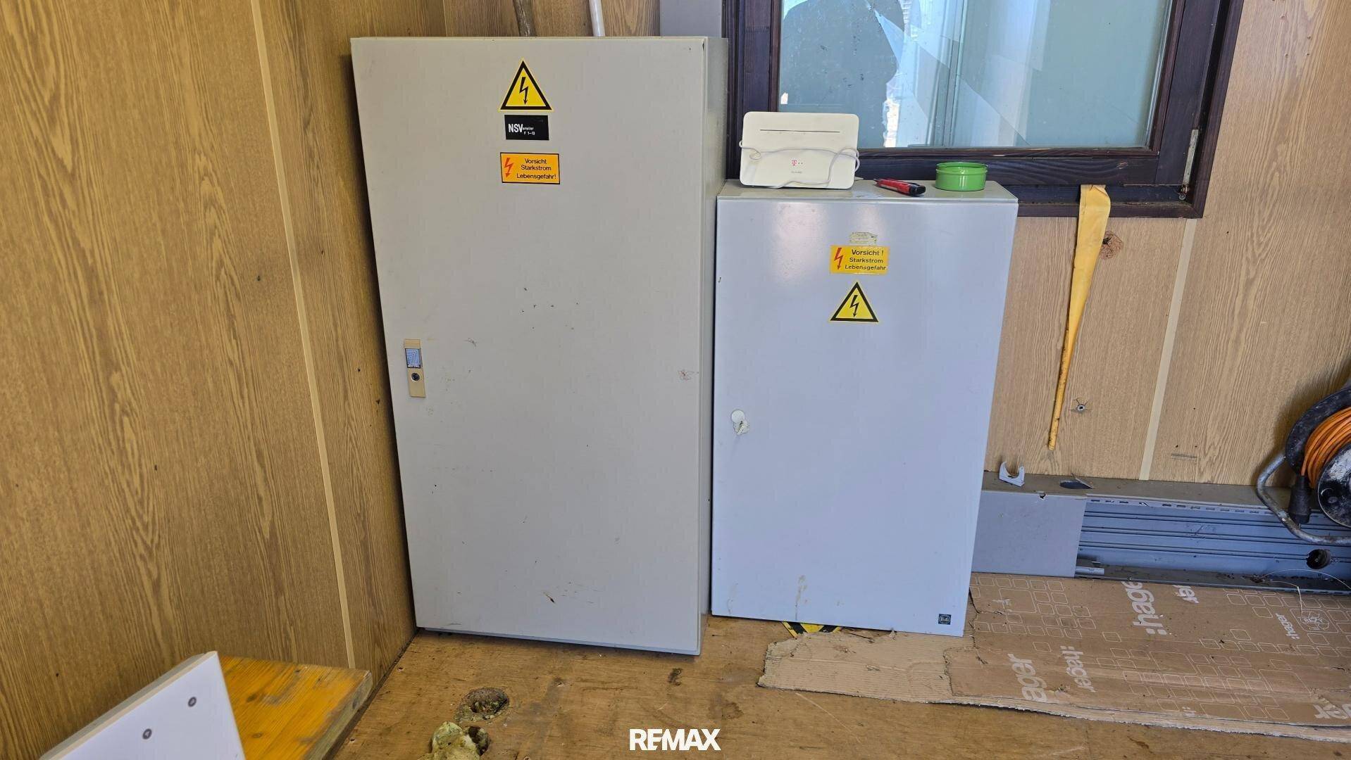 Zwei geschlossene Elektroschränke in einem Technikraum mit Holzverkleidung und einem Fenster.