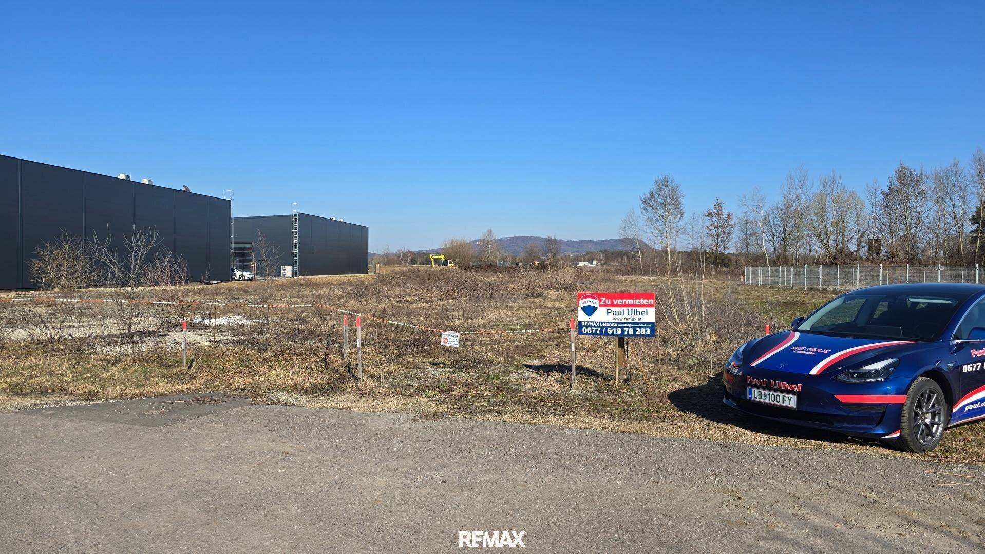 Blick auf das unbebaute Grundstück mit einem "Zu vermieten"-Schild und einem Auto im Vordergrund.