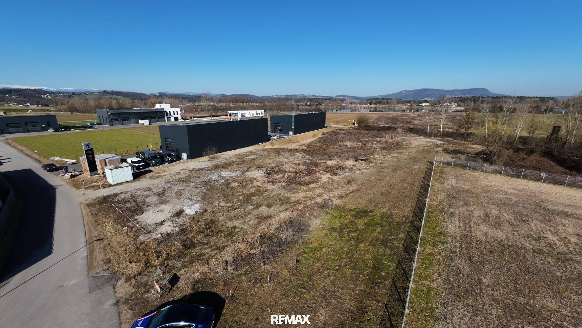 Weitläufige Ansicht des unbebauten Grundstücks mit umliegenden Gewerbegebäuden und ländlicher Landschaft.