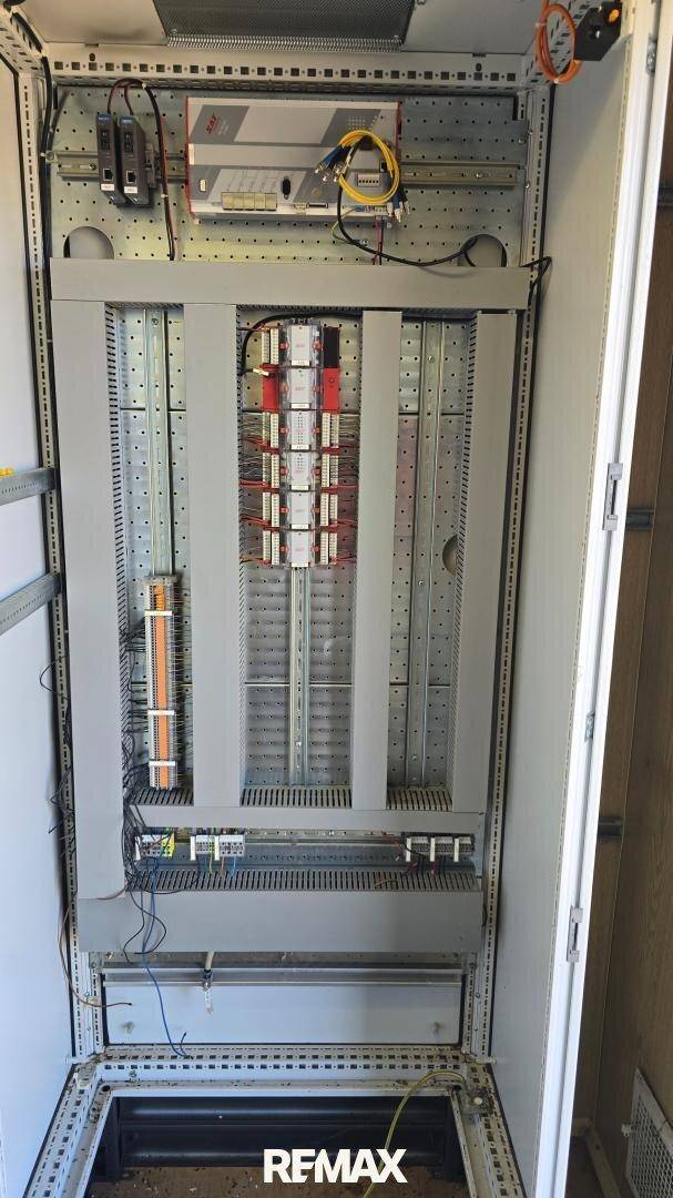 Offener Elektroschrank mit zahlreichen Kabeln und Sicherungen in einem Technikraum.