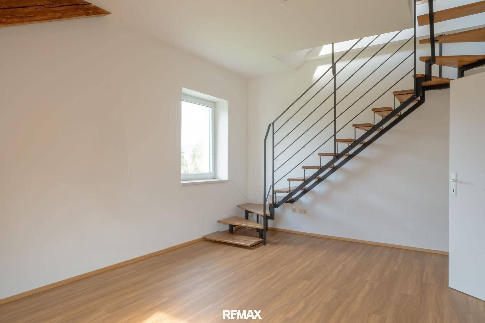 Heller Raum mit moderner offener Treppe, großem Fenster und hellem Holzfußboden.