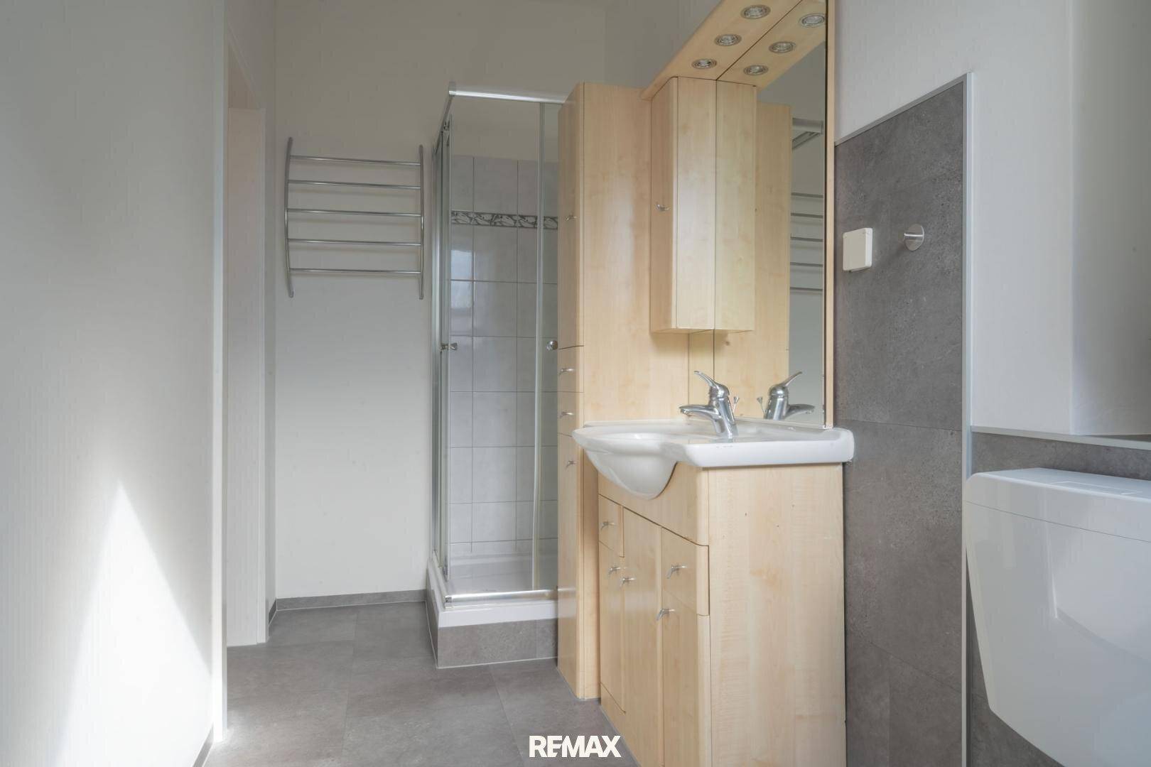 Modernes Badezimmer mit Duschkabine, Waschbecken, Holzwaschtisch und Handtuchheizkörper.