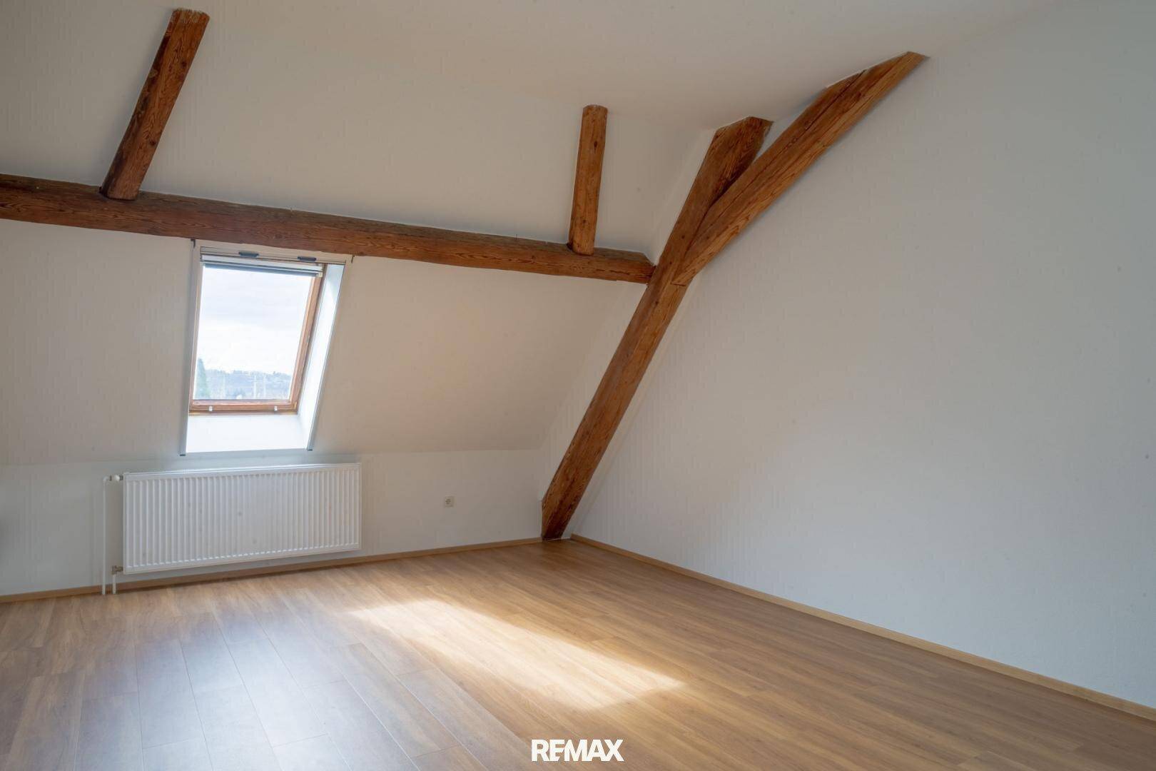 Gemütlicher Dachraum mit sichtbaren Holzbalken, Dachfenster und Heizkörper.