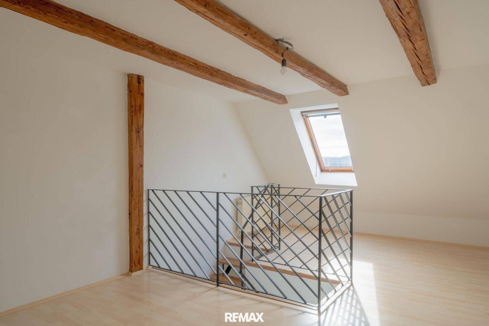 Geräumiger Dachbodenbereich mit rustikalen Holzbalken, Dachfenster und moderner Treppengalerie.