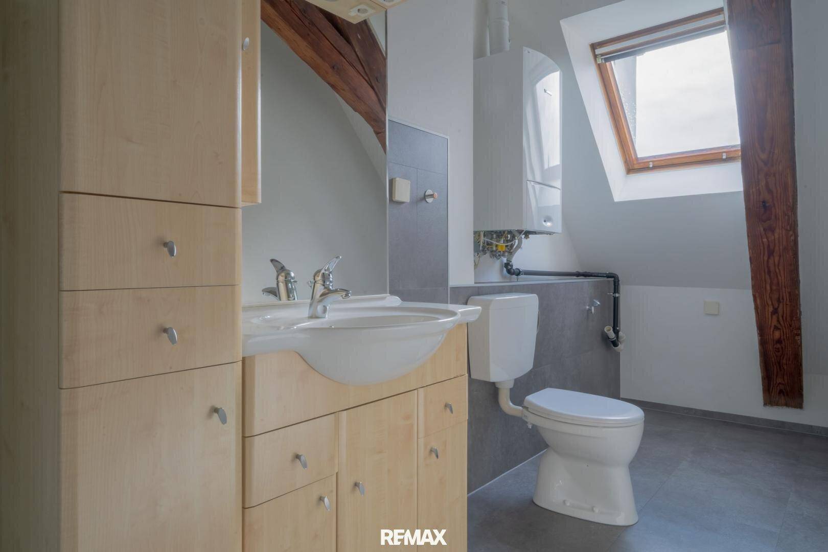 Badezimmer im Dachgeschoss mit Waschbecken, Toilette, Holzschränken und Dachfenster.