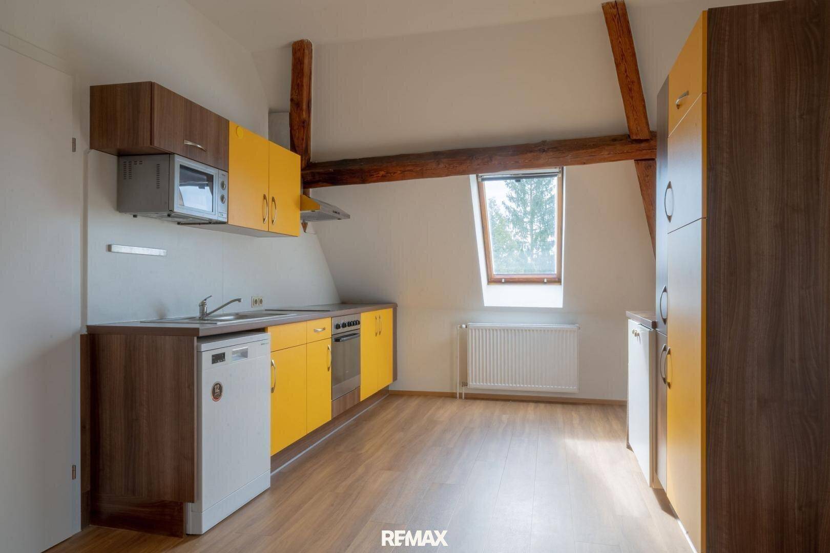 Helle Dachgeschossküche mit gelben Schränken, Holzbalken und Dachfenster.