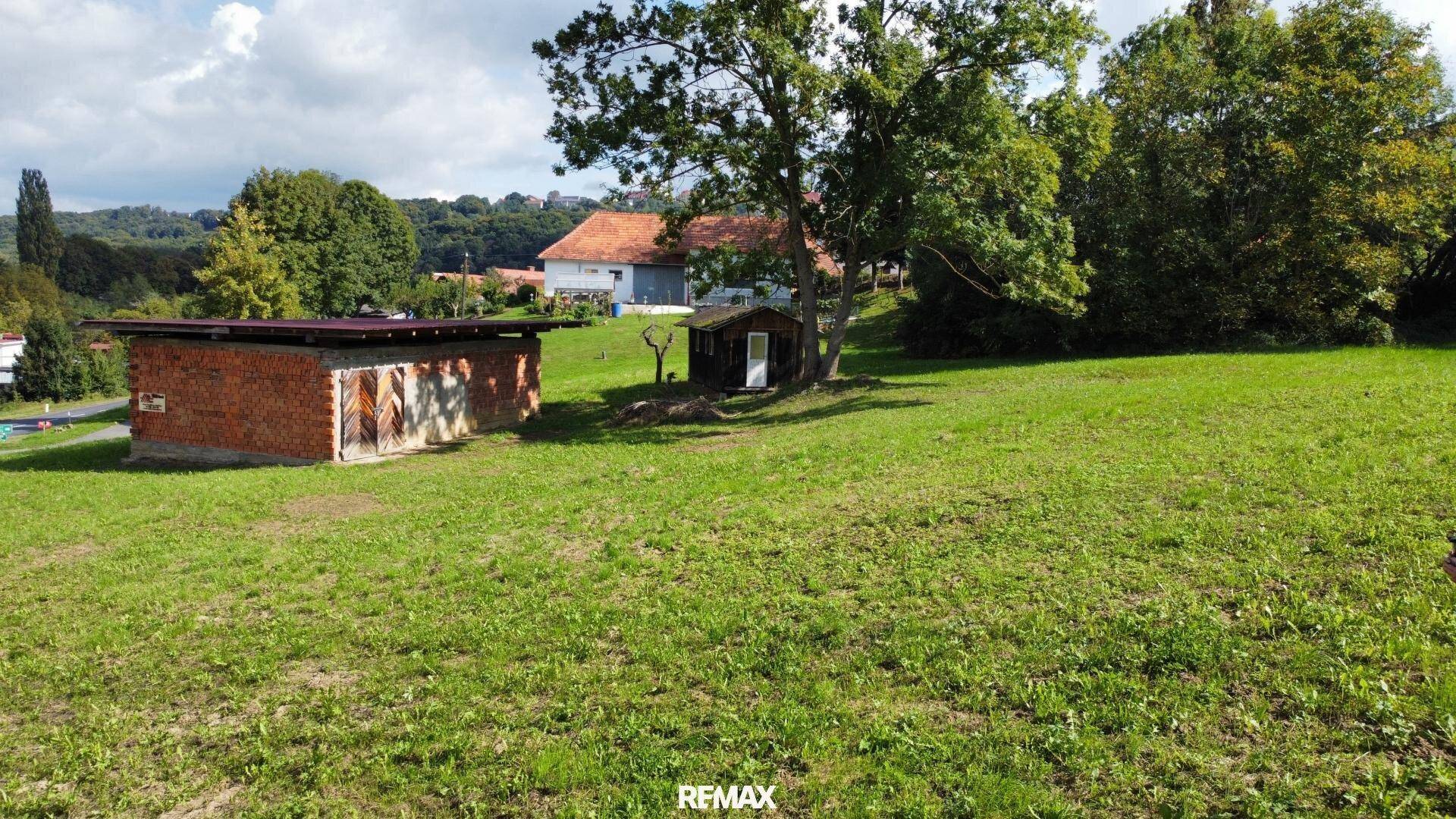 Großes grünes Grundstück mit einem Ziegelgebäude und einem Holzschuppen, umgeben von ländlicher Idylle.