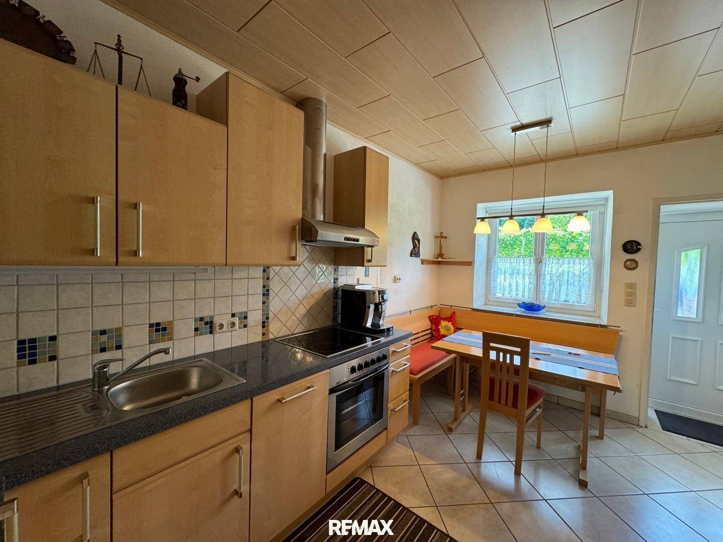 Einbauküche mit Holzelementen, Fliesenboden und Essbereich am Fenster.