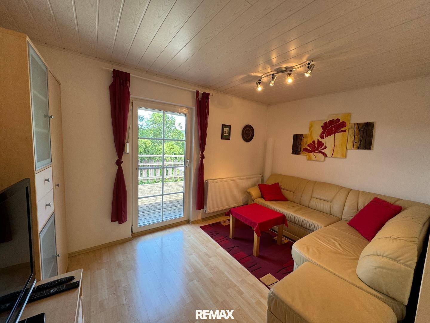 Gemütliches Wohnzimmer mit beigem Sofa, rotem Teppich und Balkonzugang.