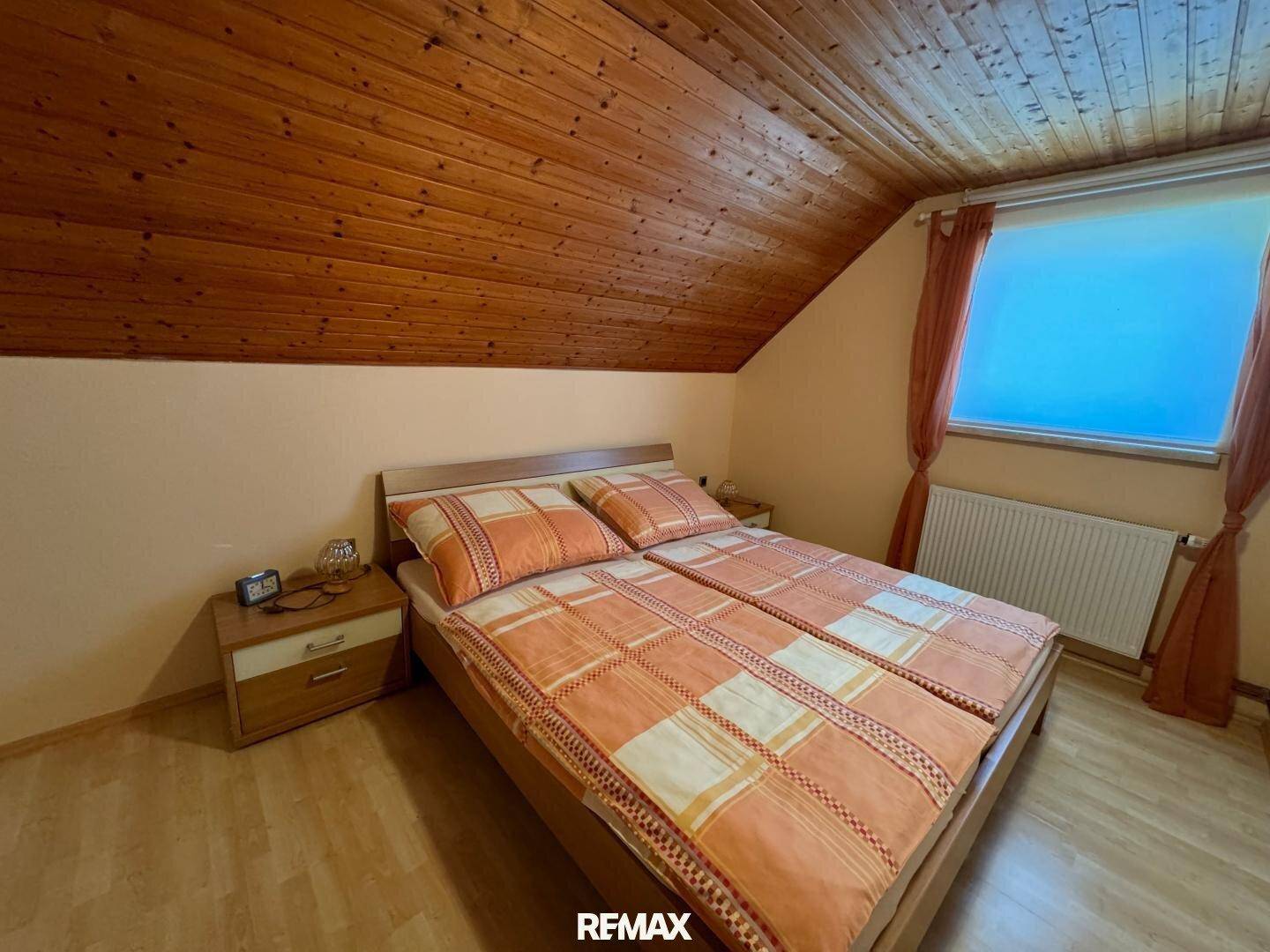 Schlafzimmer mit Doppelbett, Holzdecke und Laminatboden unter Dachschrägen.