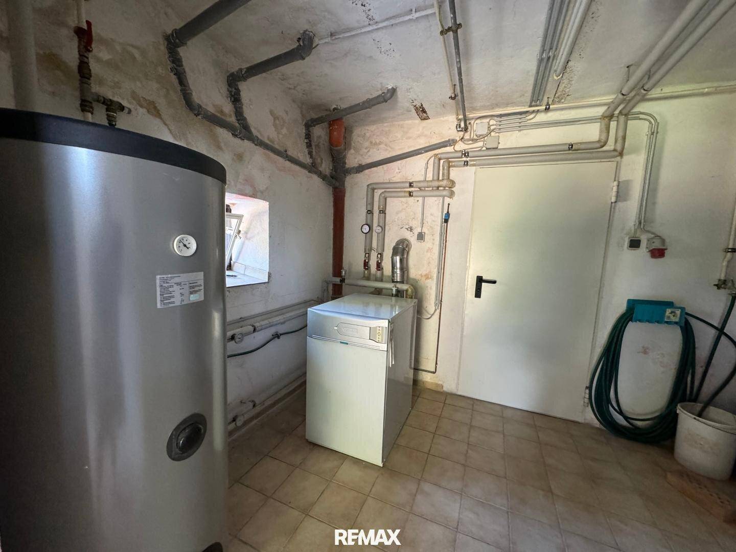 Technikraum im Keller mit Heizungsanlage, Warmwasserspeicher und Waschmaschine.