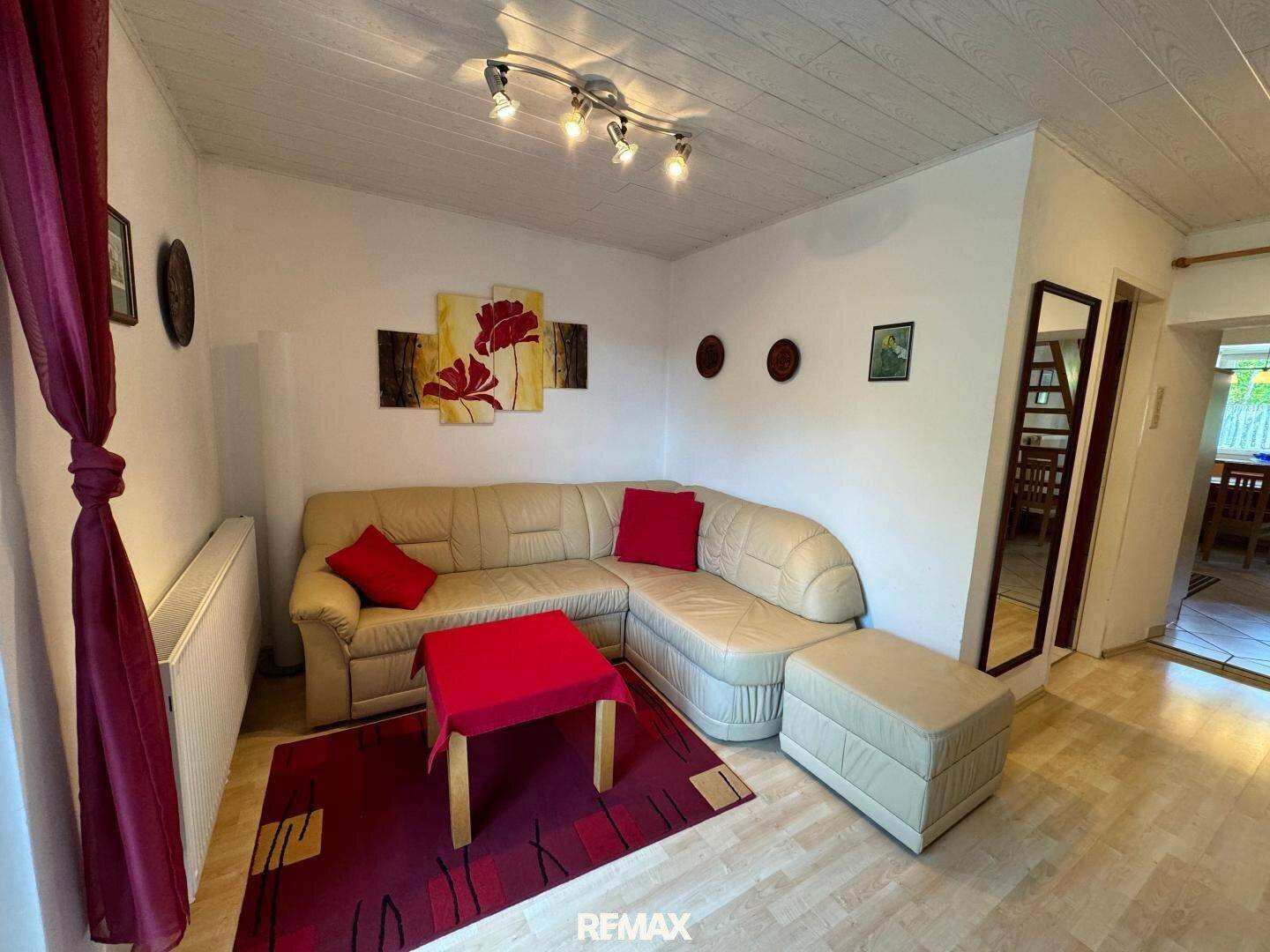 Heller Wohnbereich mit beigem Sofa, rotem Couchtisch und Wanddekoration.