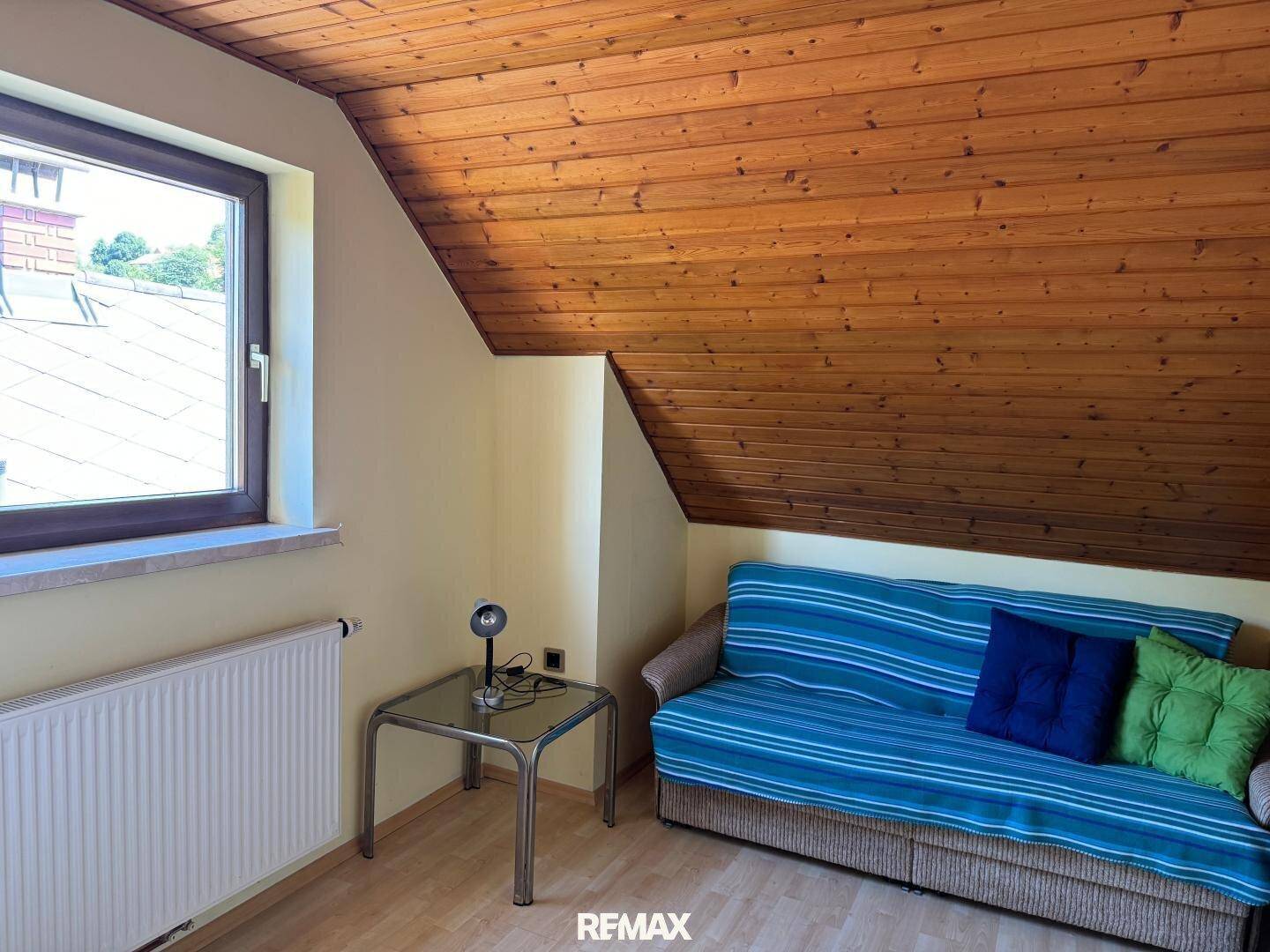 Gemütliches Zimmer mit Schlafsofa, Holzdecke und Fenster unter der Dachschräge.