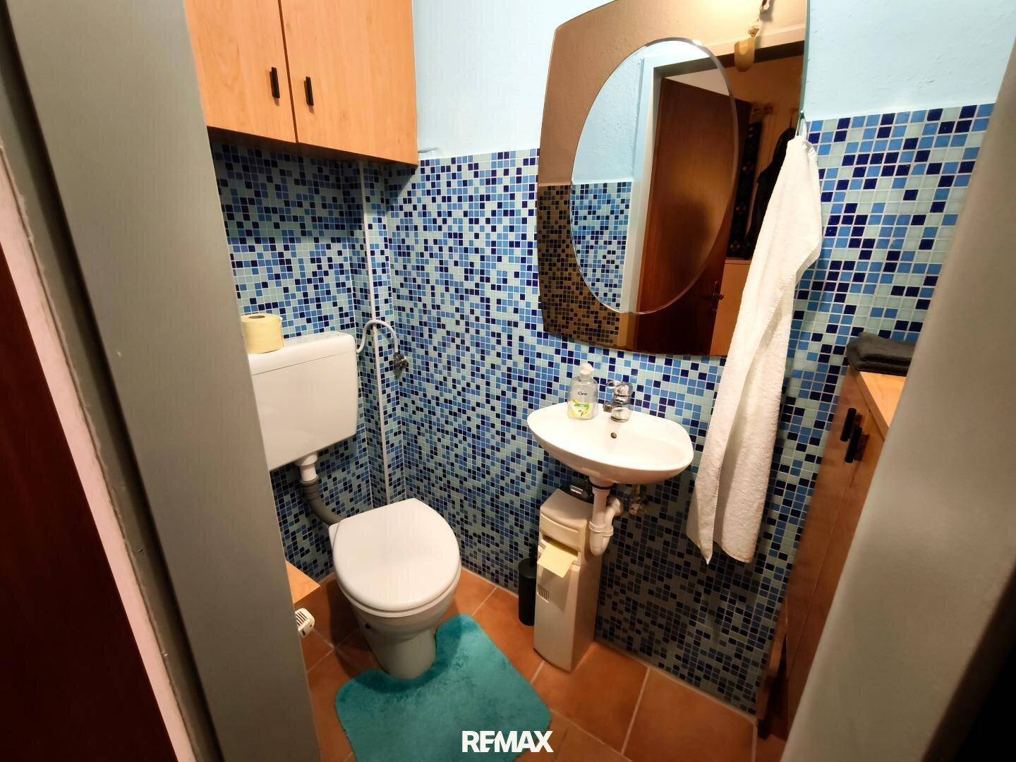 Kleines WC mit Mosaikfliesen in Blautönen, Waschbecken und Toilette.