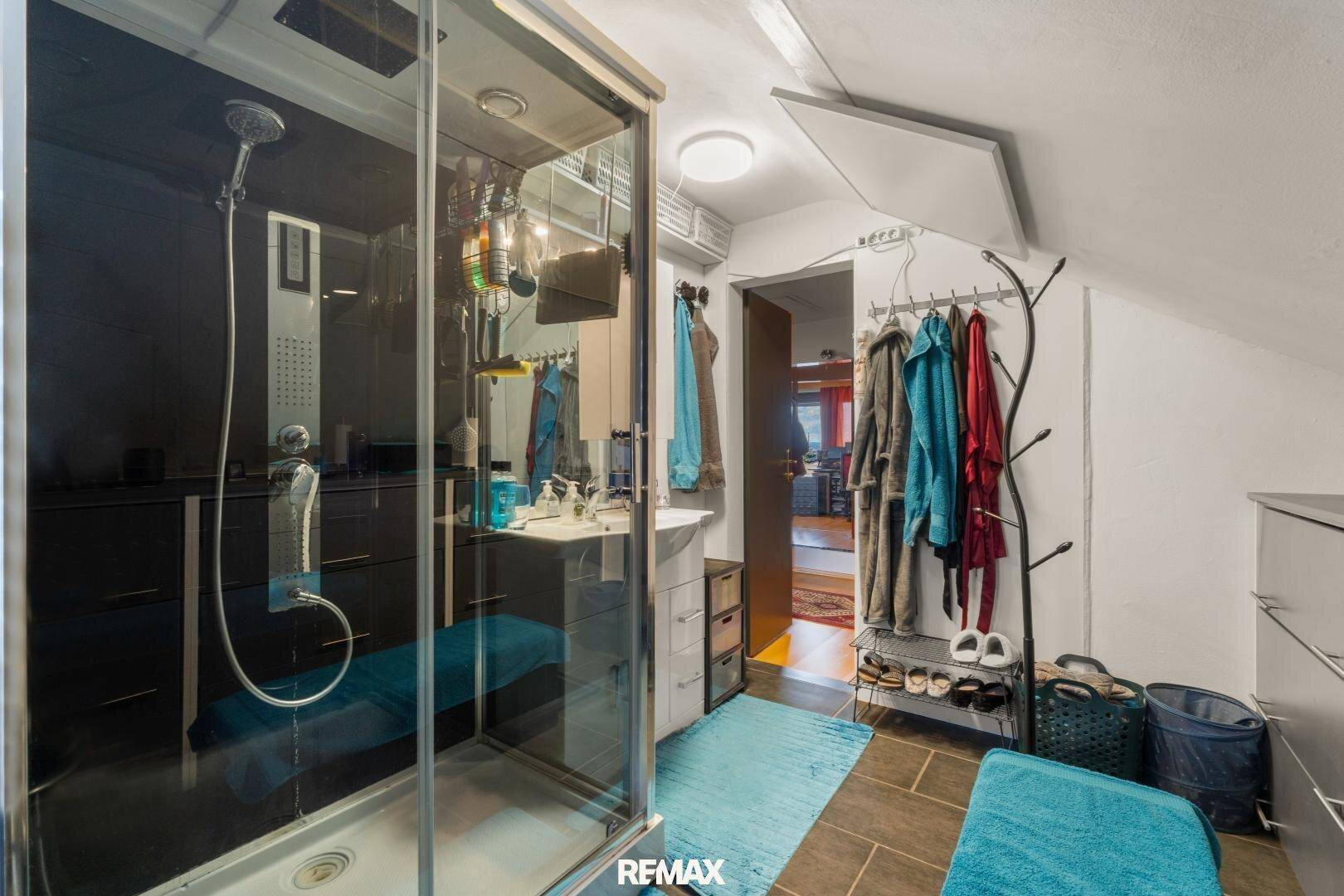 Badezimmer im Dachgeschoss mit Duschkabine, Waschbecken und Stauraum, unter einer Dachschräge.