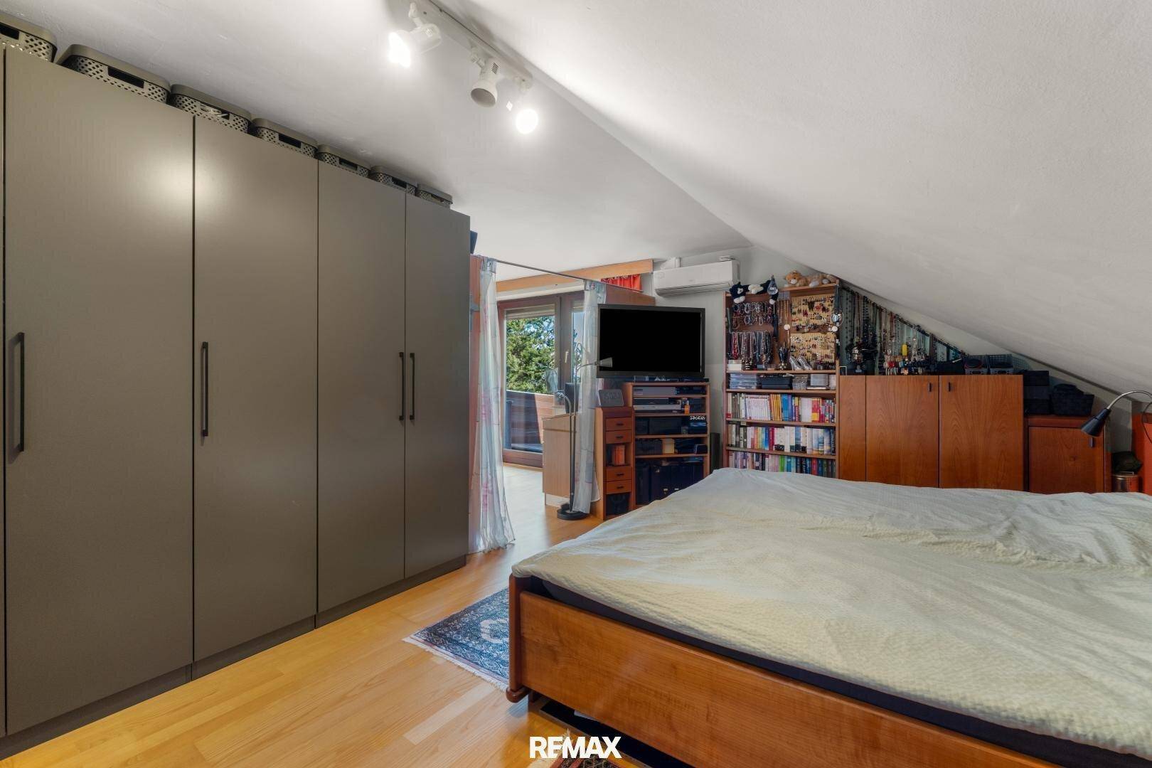 Schlafzimmer im Dachgeschoss mit großem Kleiderschrank, Holzbett und Zugang zu einem Balkon.