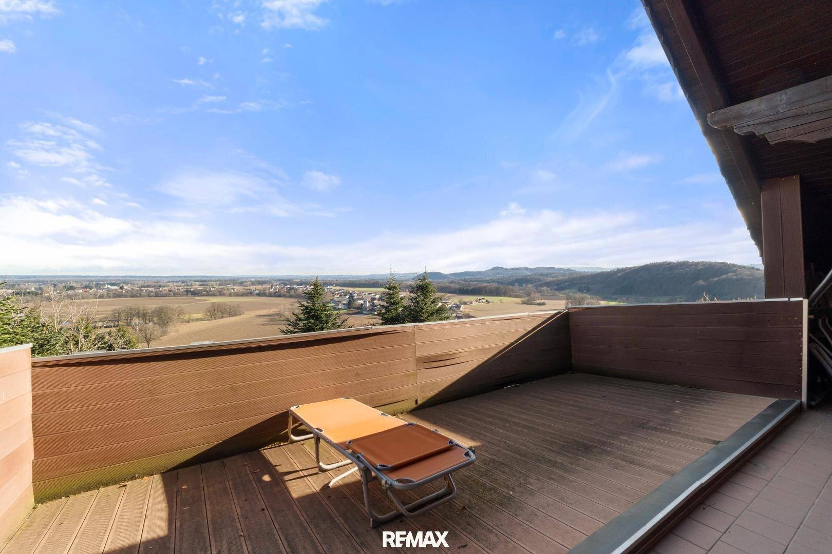 Geräumiger Balkon mit Holzbelag und Liegestuhl, bietet einen weiten Blick über die Landschaft.