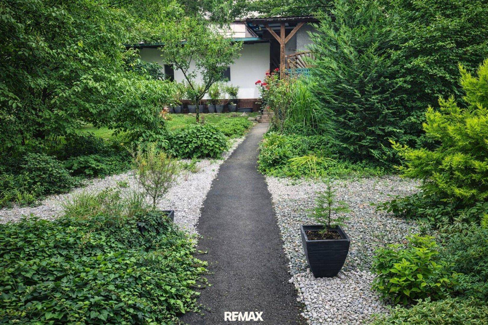 Gepflegter Gartenweg umgeben von üppigem Grün und verschiedenen Pflanzen.