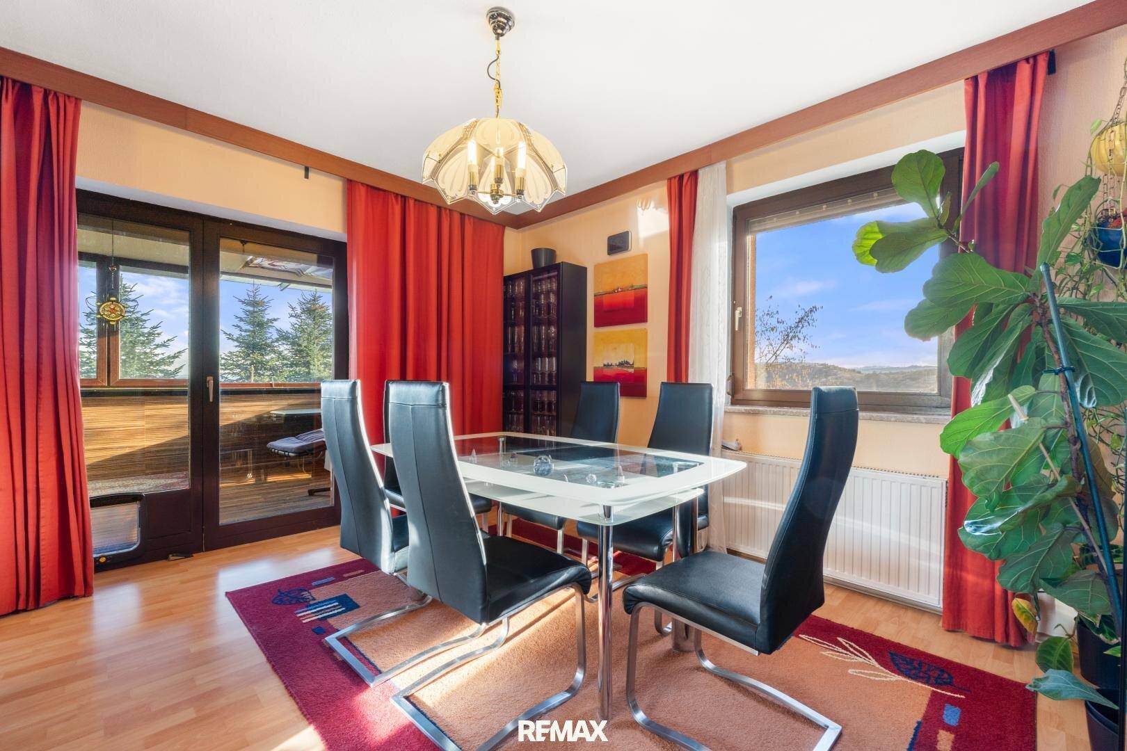 Helles Esszimmer mit Holzboden, Glastisch, schwarzen Stühlen und Zugang zu einem Balkon mit Weitblick.