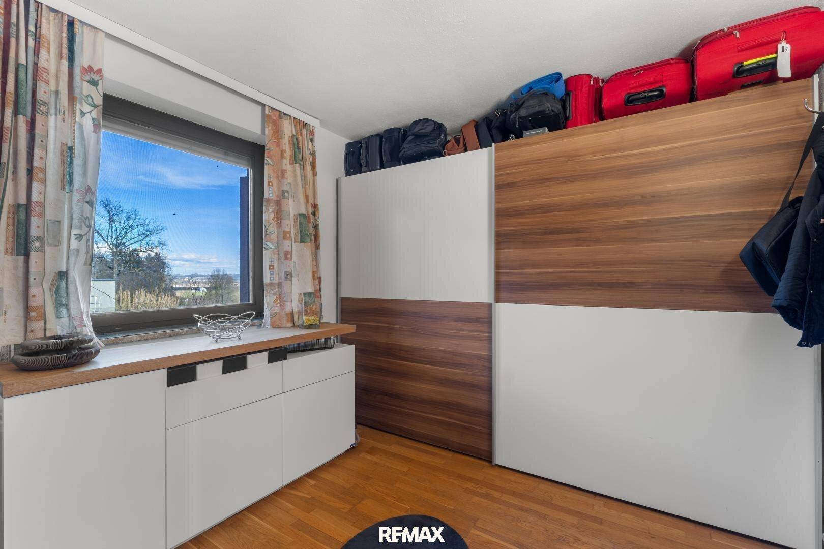 Raum mit Holzboden, großen Schiebetürenschränken und einem Fenster, das Tageslicht hereinlässt.