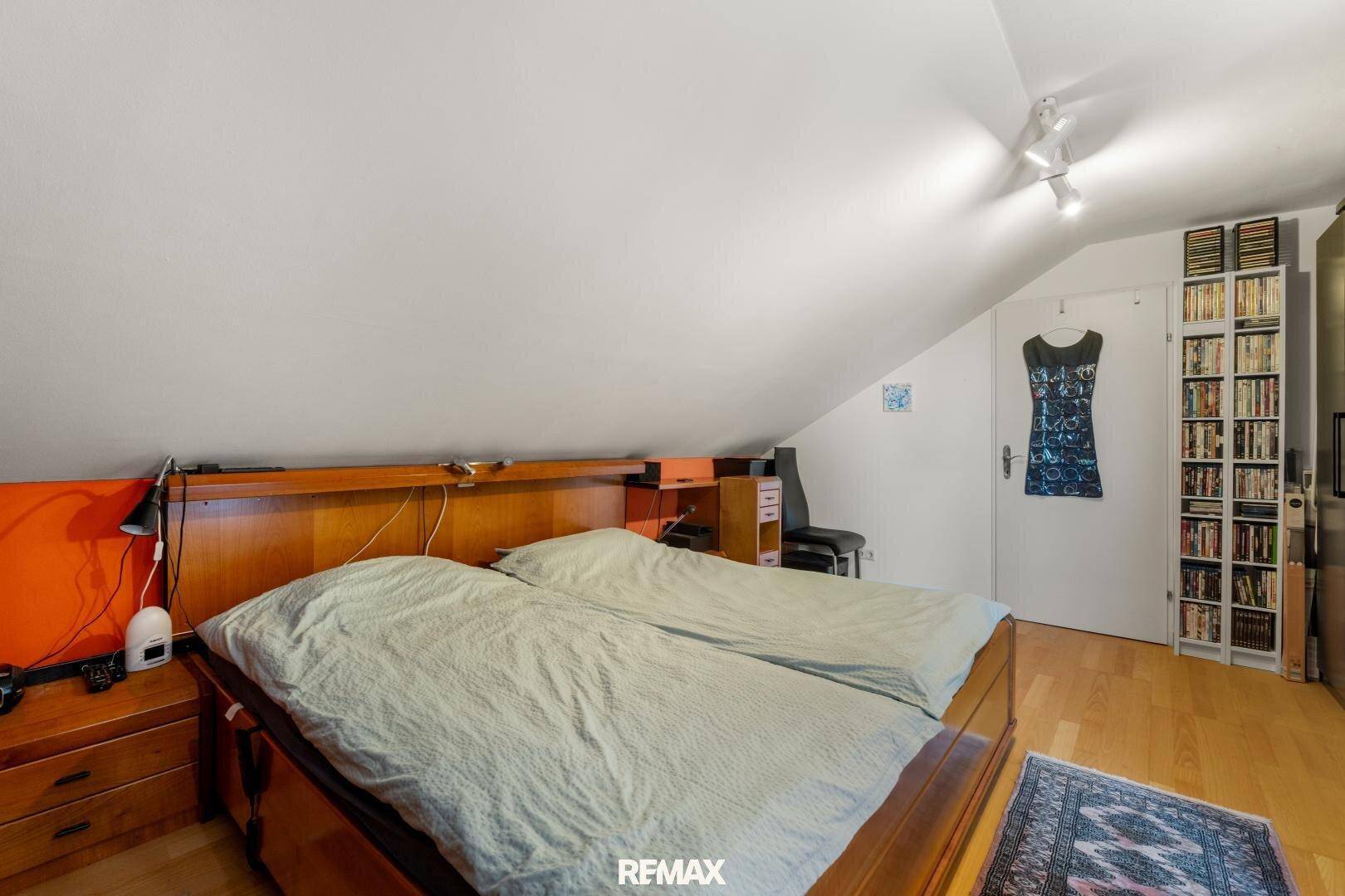 Schlafzimmer im Dachgeschoss mit Holzbett, schrägen Wänden und einem Bücherregal.