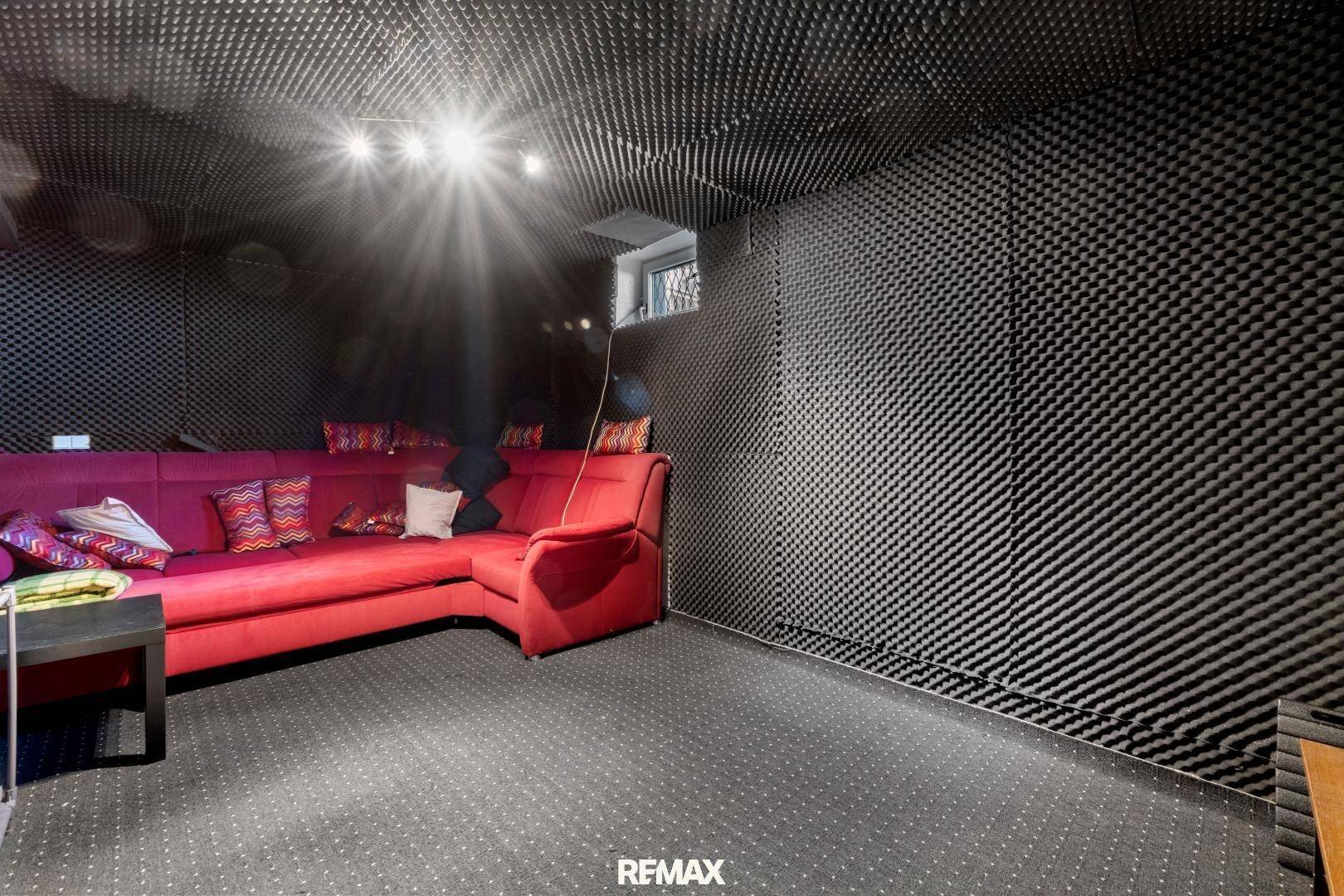 Gemütlicher Medienraum mit rotem Sofa und schallabsorbierenden Wänden, perfekt zum Entspannen.