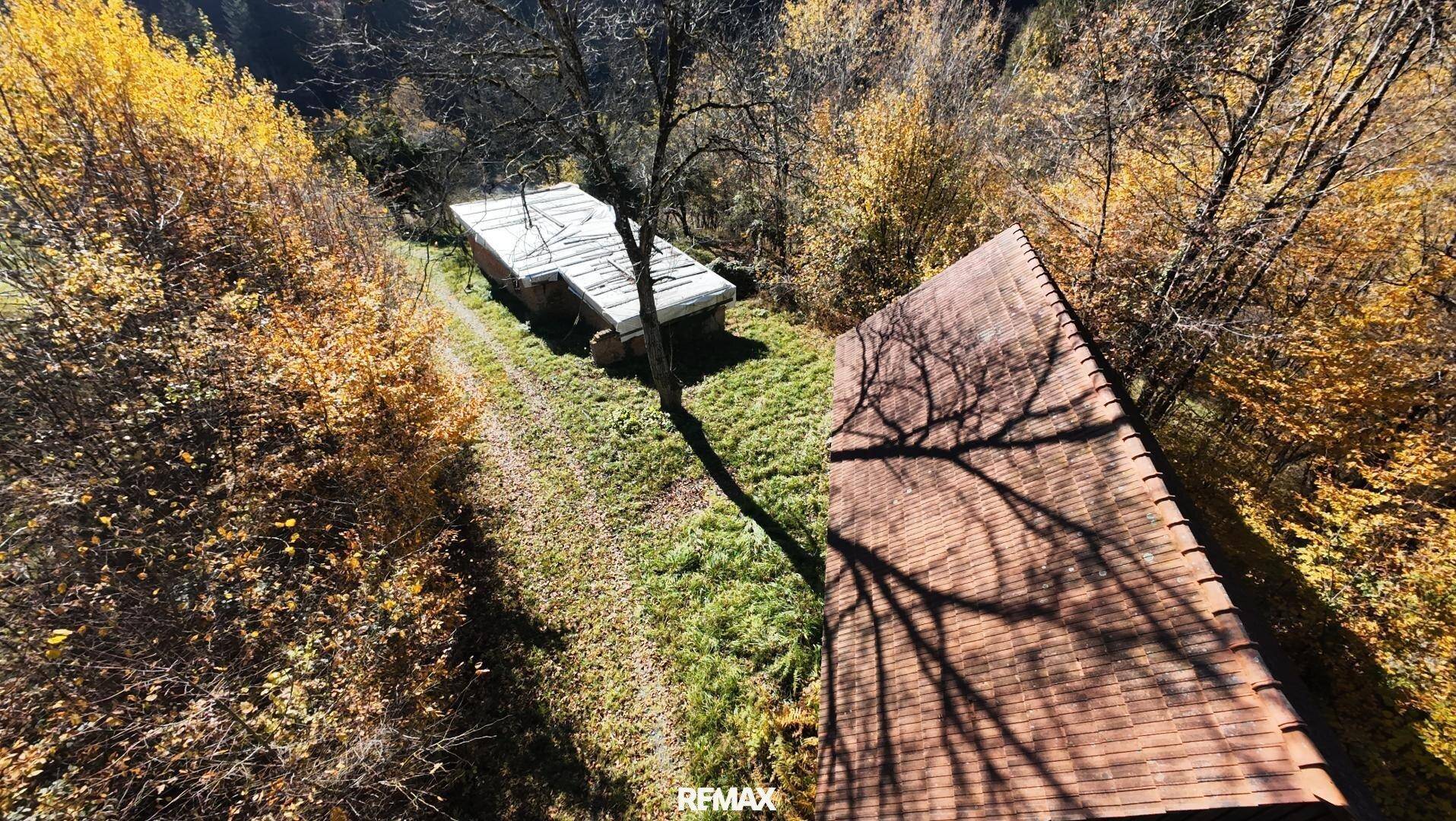 Blick von oben auf ein Ziegeldach und ein weiteres Gebäude, umgeben von herbstlichen Bäumen.