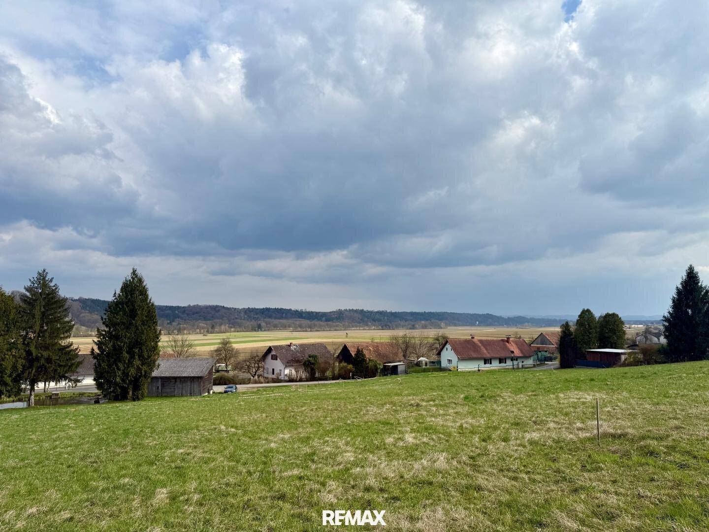 Weitläufiges grünes Grundstück mit Blick auf eine ländliche Bebauung und bewölkten Himmel.