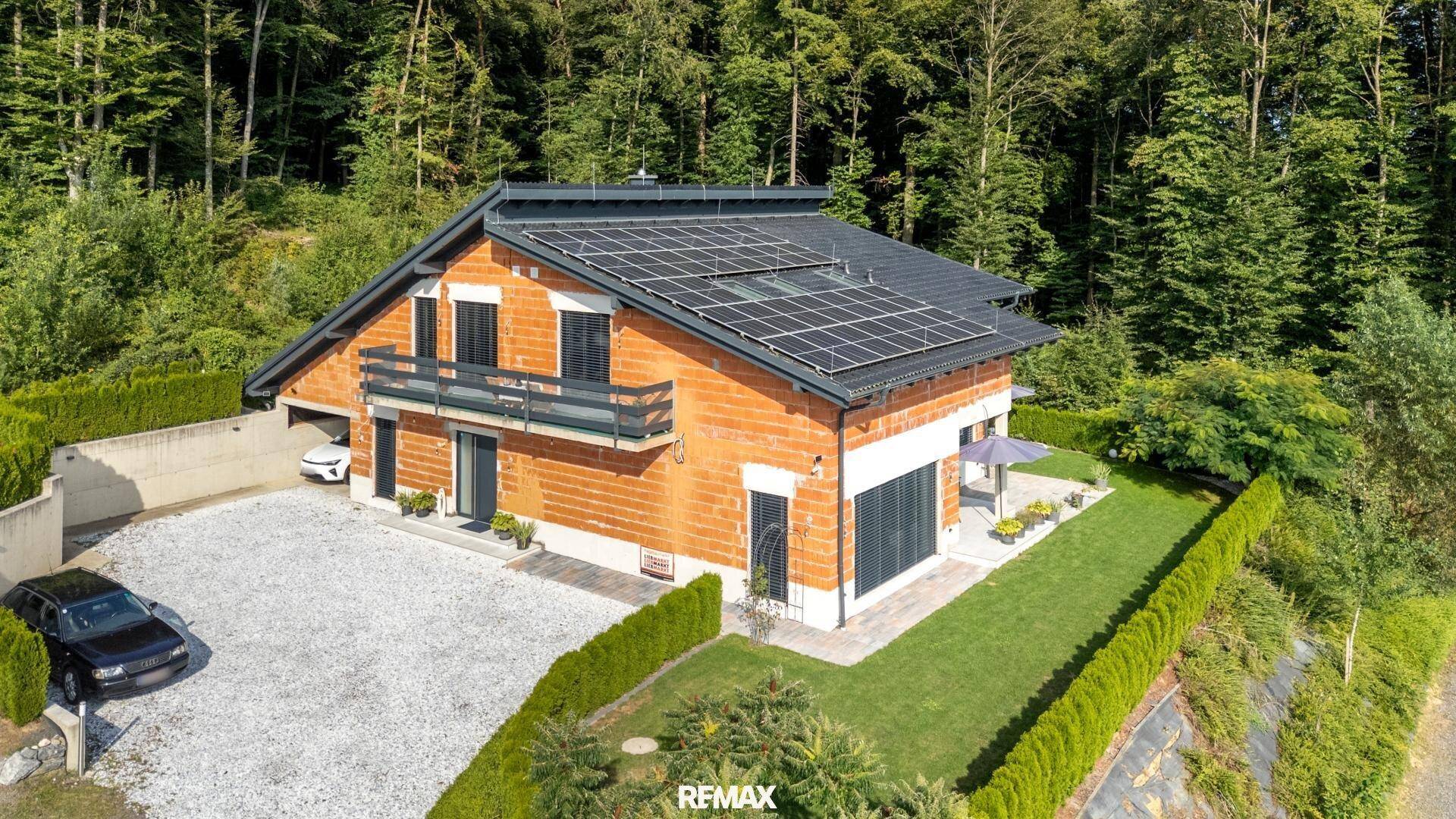 Drohnenaufnahme des modernen Hauses mit Solaranlage und gepflegtem Gartenbereich unter blauem Himmel.
