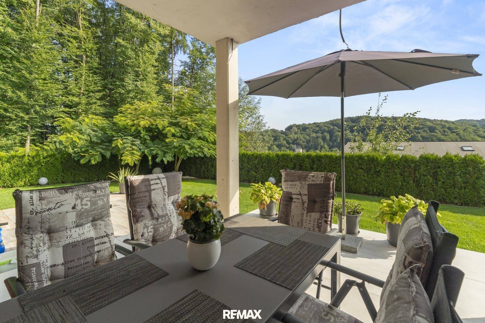 Gemütliche Terrasse mit Esstisch, Sonnenschirm und umgeben von üppigem Grün.