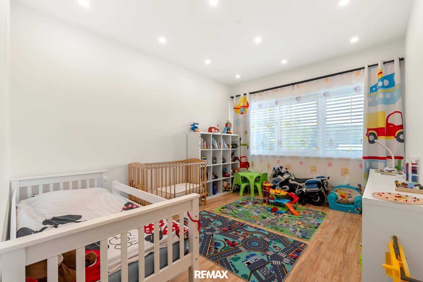 Helles Kinderzimmer mit zwei Betten, Spielbereich und großem Fenster.
