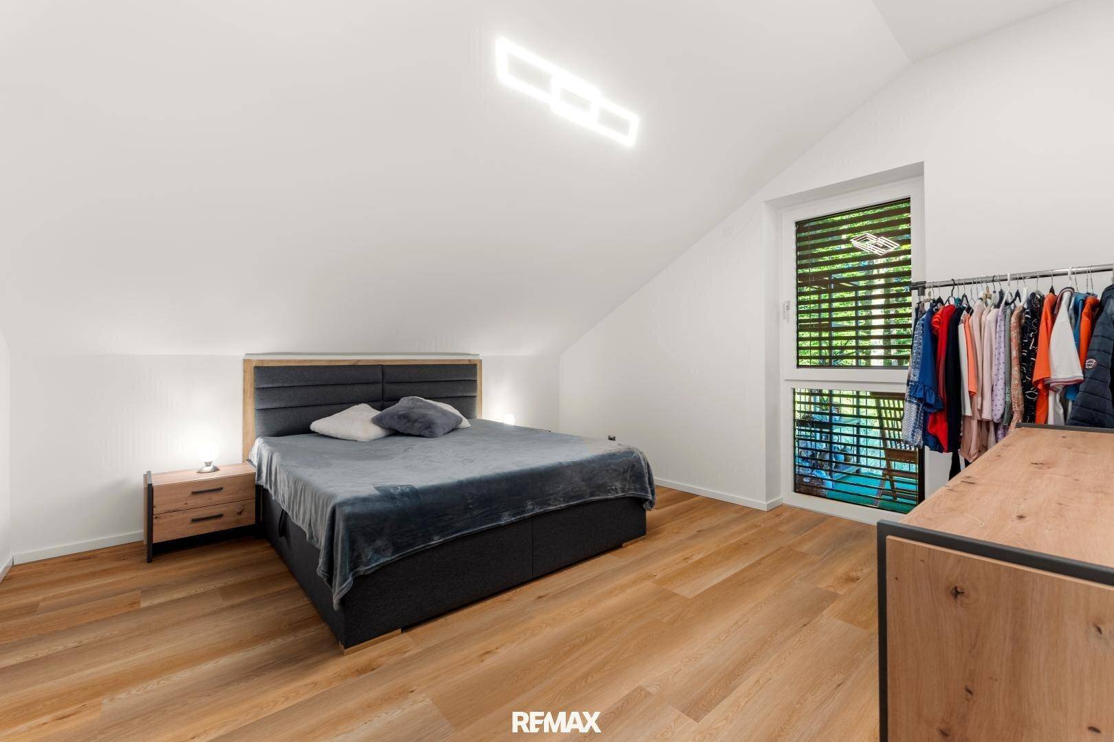 Schlafzimmer im Dachgeschoss mit Holzboden, Doppelbett und Fenster mit Blick ins Grüne.