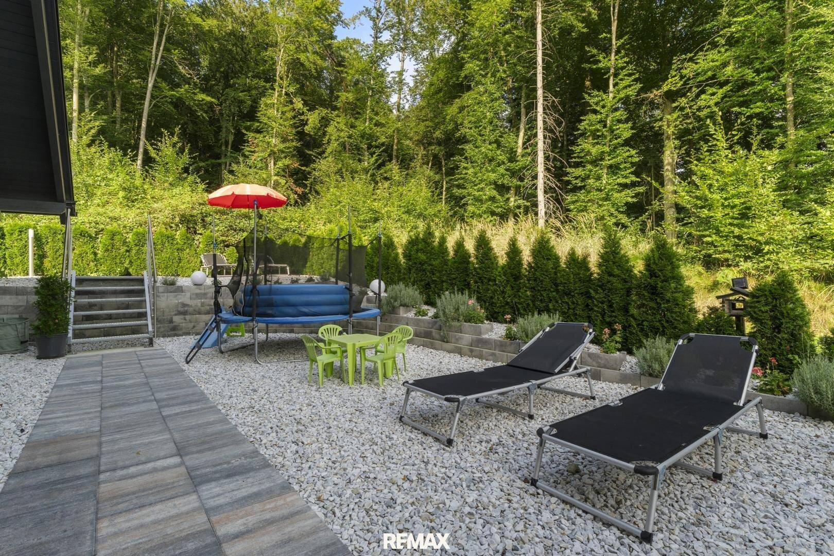 Geräumige Terrasse mit Liegestühlen und Spielbereich, umgeben von Bäumen und Hecken.