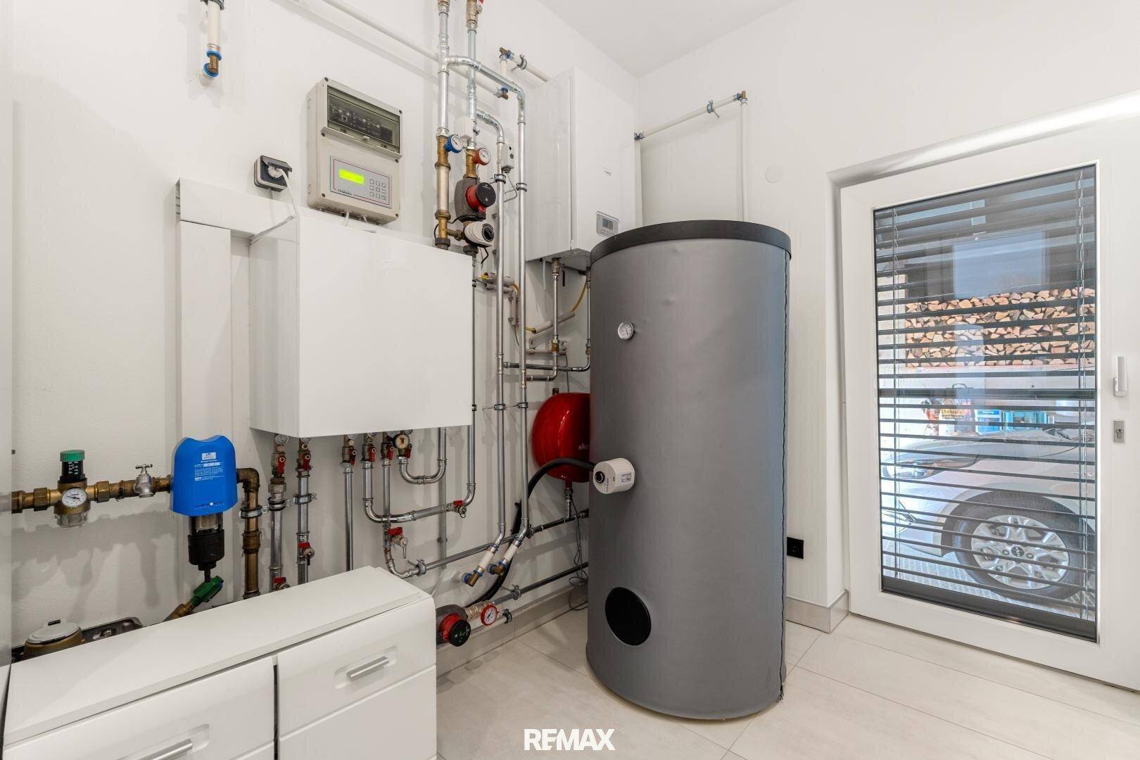 Technikraum mit Heizungsanlage, Warmwasserspeicher und Zugang nach draußen.