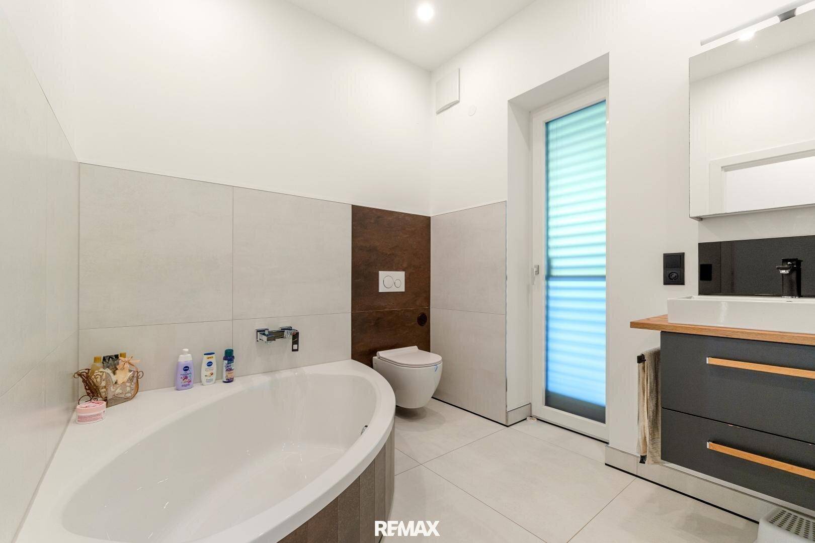 Modernes Badezimmer mit Badewanne, Wand-WC und Fenster für Tageslicht.
