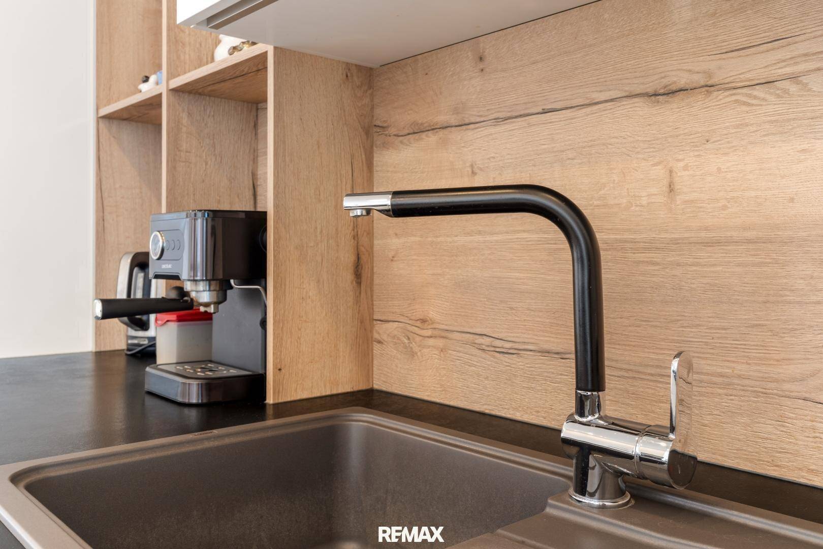 Detailansicht der modernen Küchenspüle mit schwarzem Wasserhahn und Holzwandverkleidung.