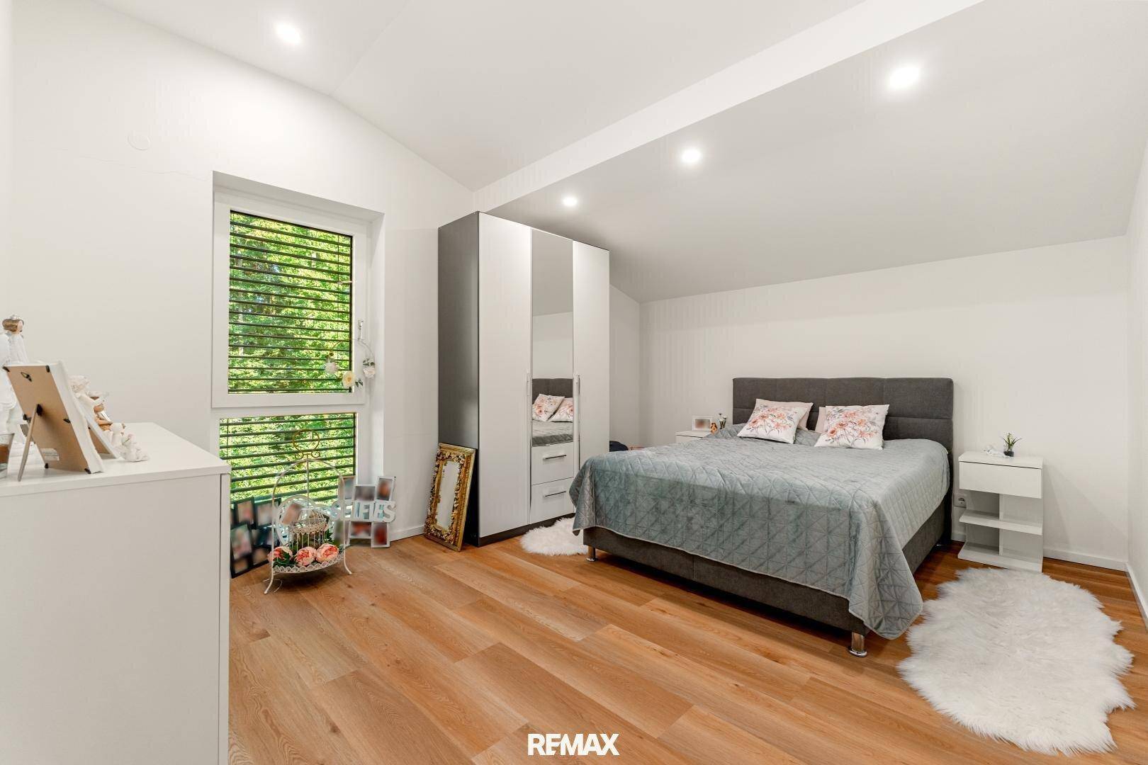 Helles Schlafzimmer mit Holzboden, Kleiderschrank und Fenster mit Blick ins Grüne.