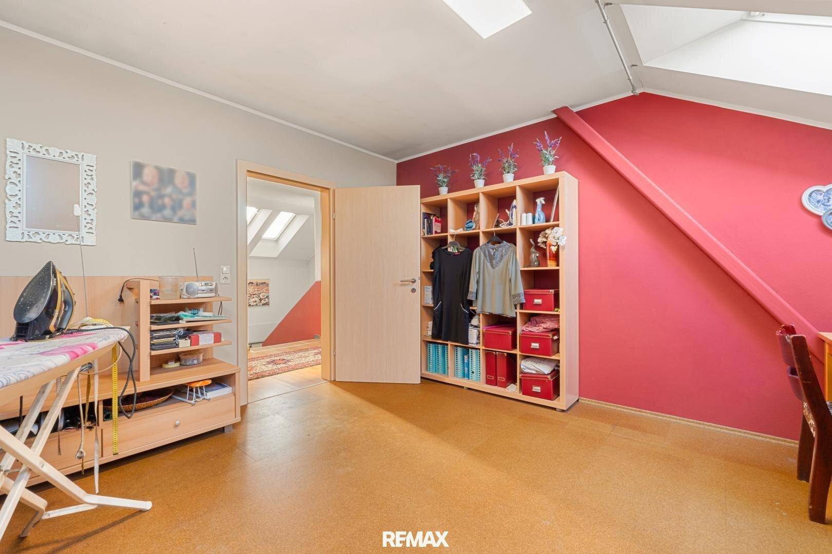 Geräumiges Hobbyzimmer mit Regalen, Bügelbrett und Zugang zu weiteren Räumen.