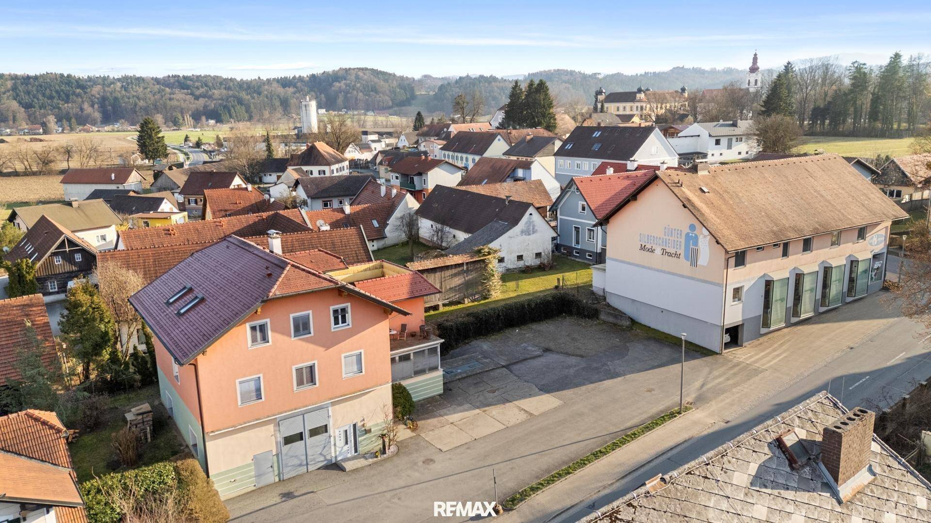 Luftaufnahme des Hauses in einer ländlichen Siedlung mit weiteren Gebäuden und Kirche im Hintergrund.