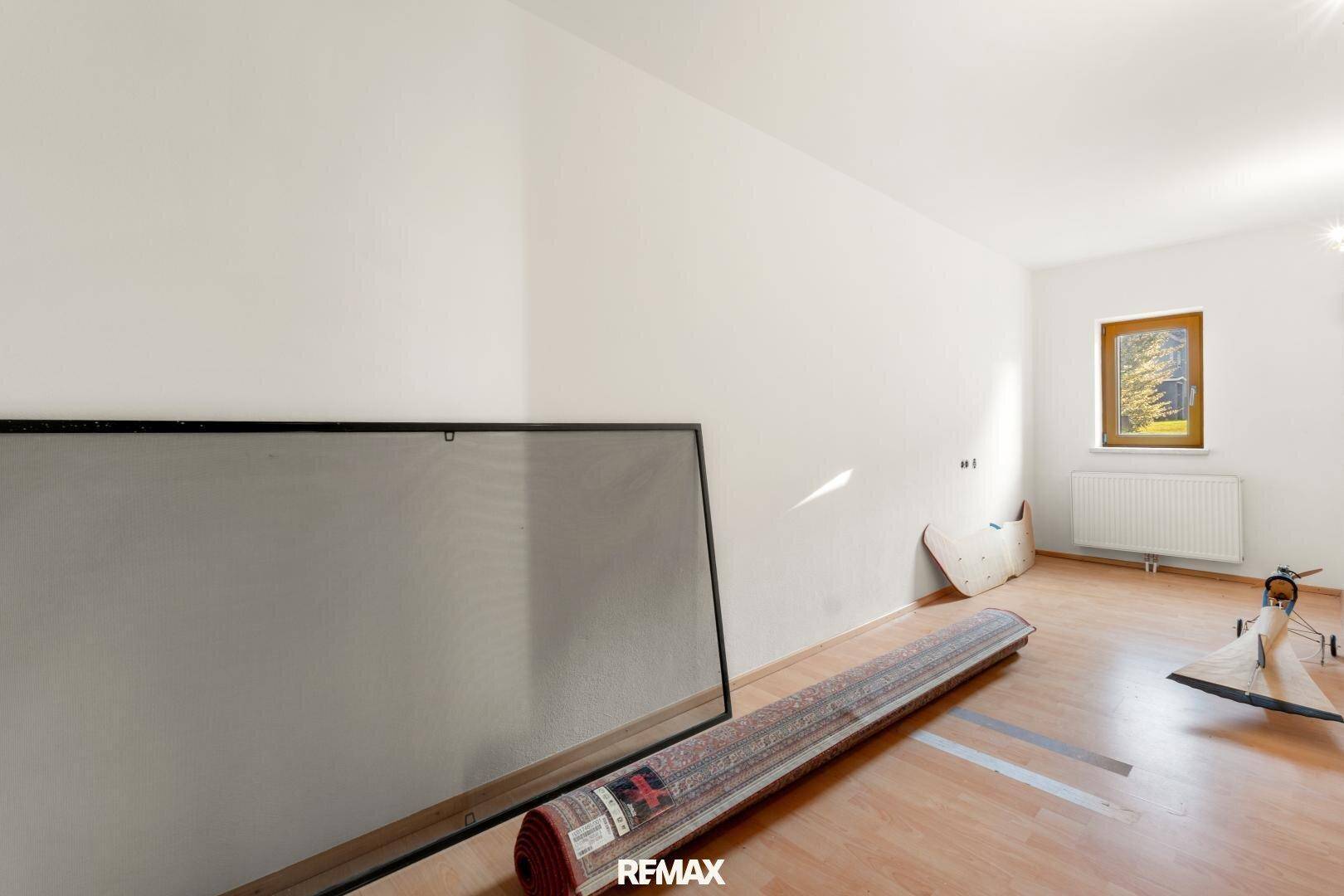 Leerer Raum mit Holzboden, Fenster und gelagertem Teppich.