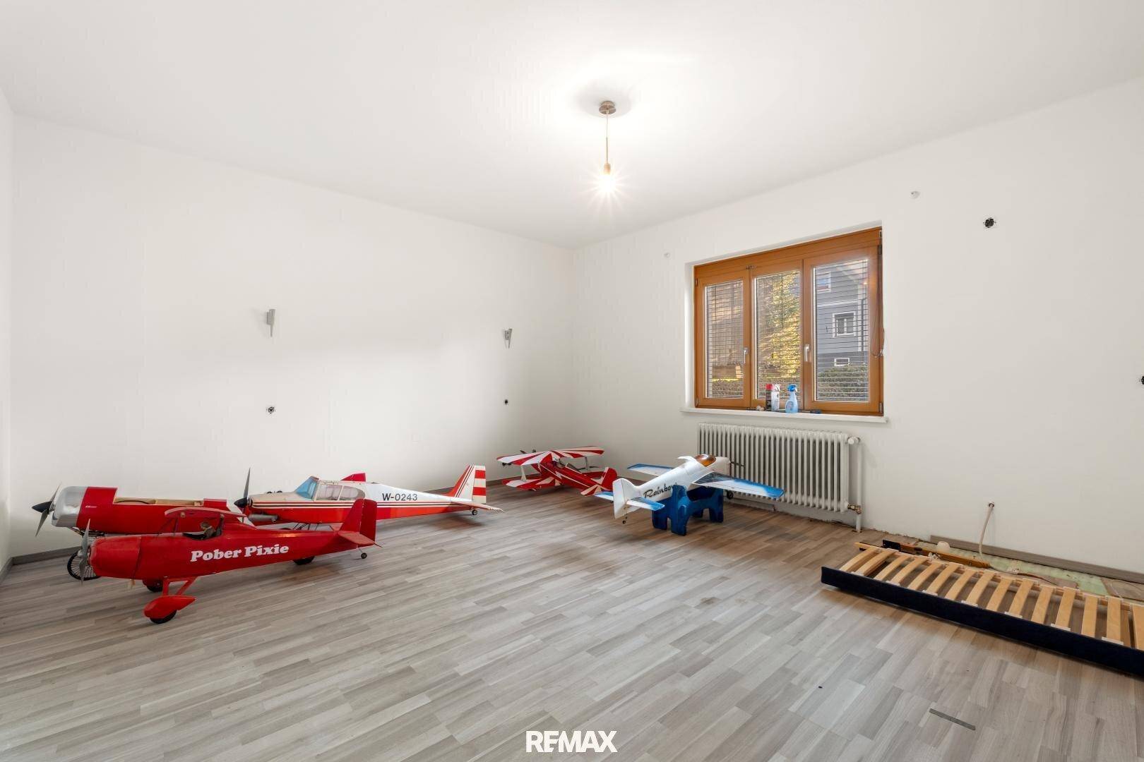 Helles Zimmer mit Holzboden, Fenster und Modellflugzeugen.