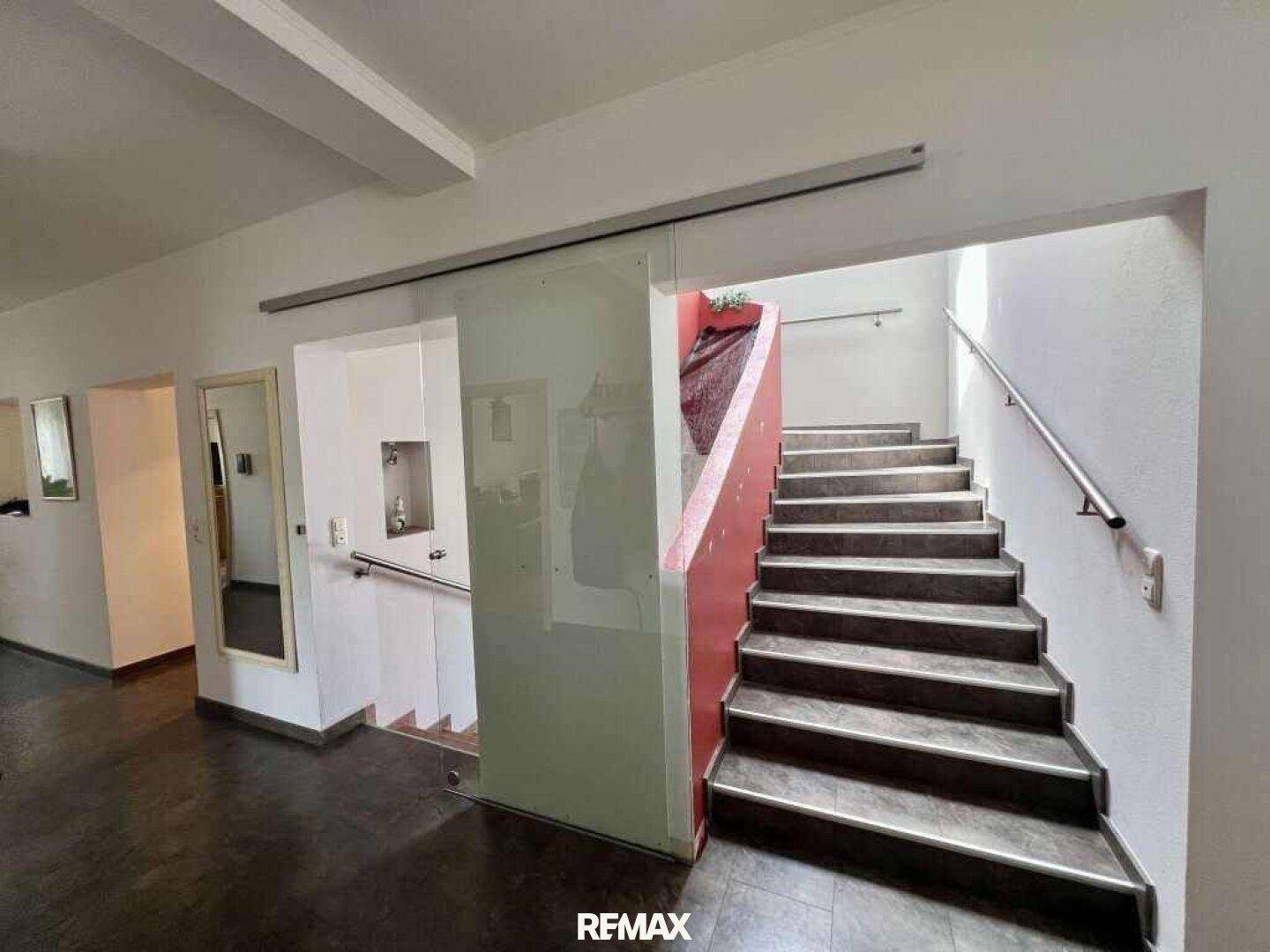 Eingangsbereich mit Treppe, Glaswand und Spiegel, der den Raum optisch vergrößert.