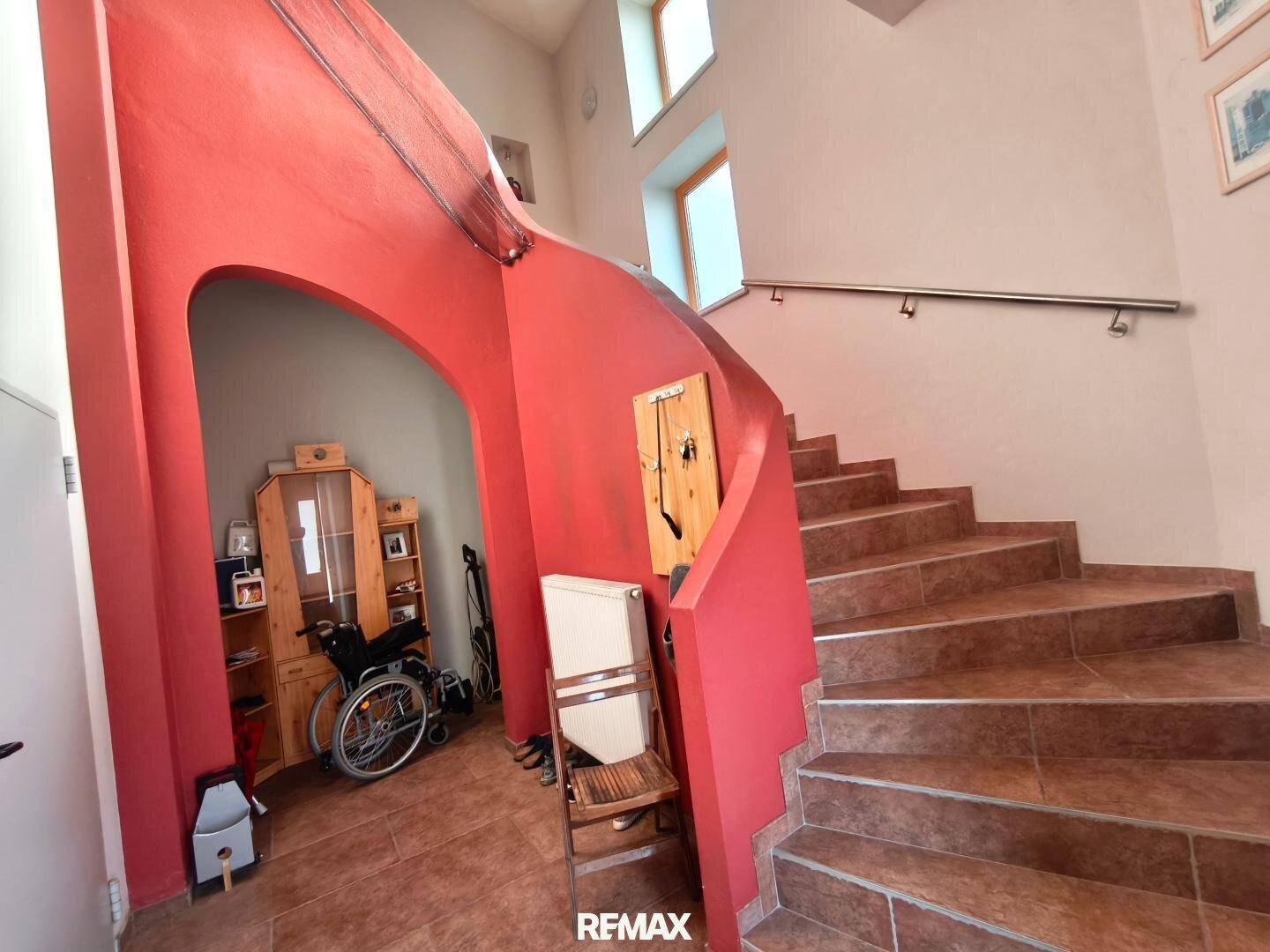 Geräumiger Flur mit gefliestem Boden und einer geschwungenen Treppe mit roter Wand.