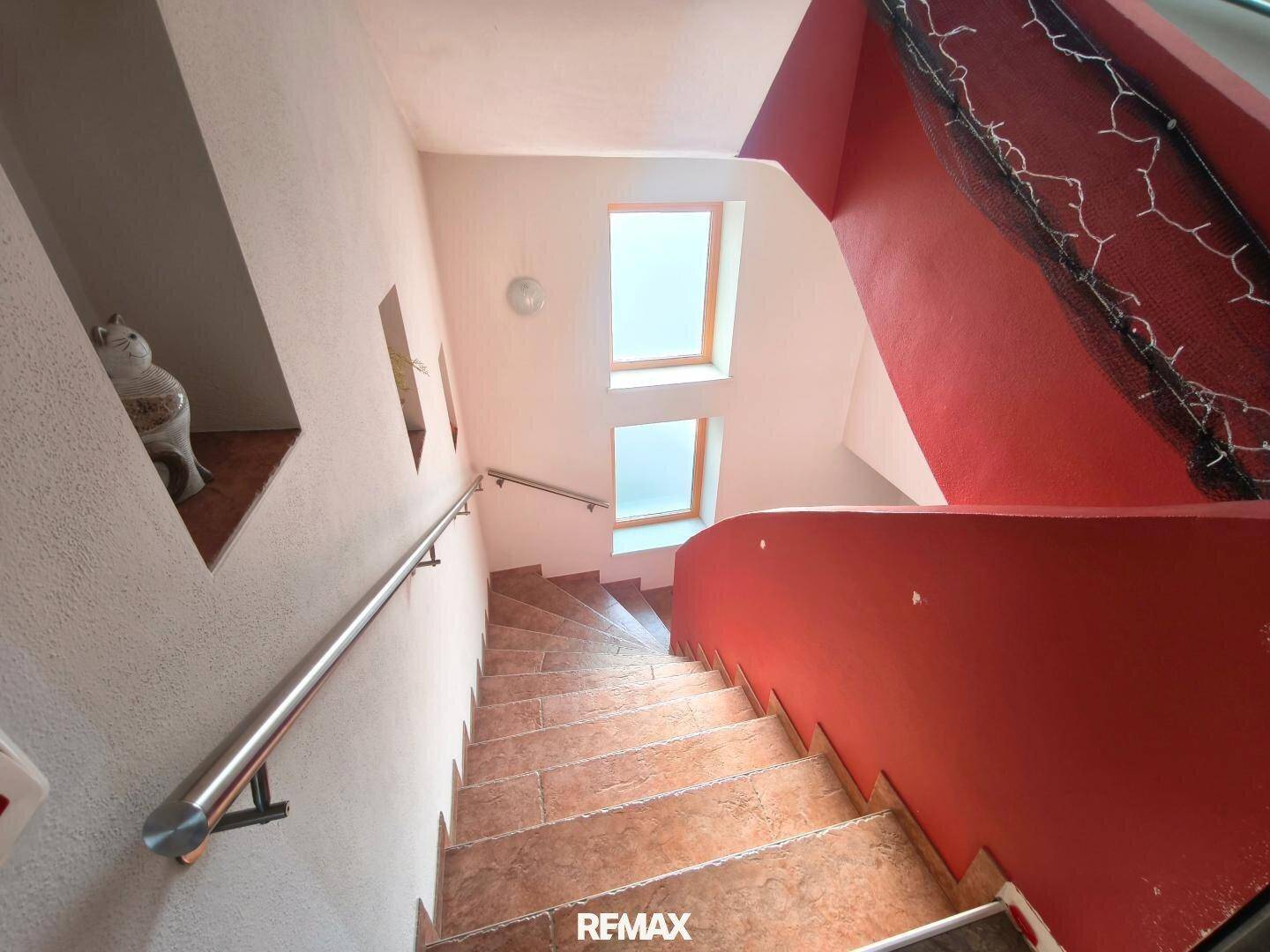 Treppenhaus mit gefliesten Stufen, roter Wand und Fenstern für natürliches Licht.